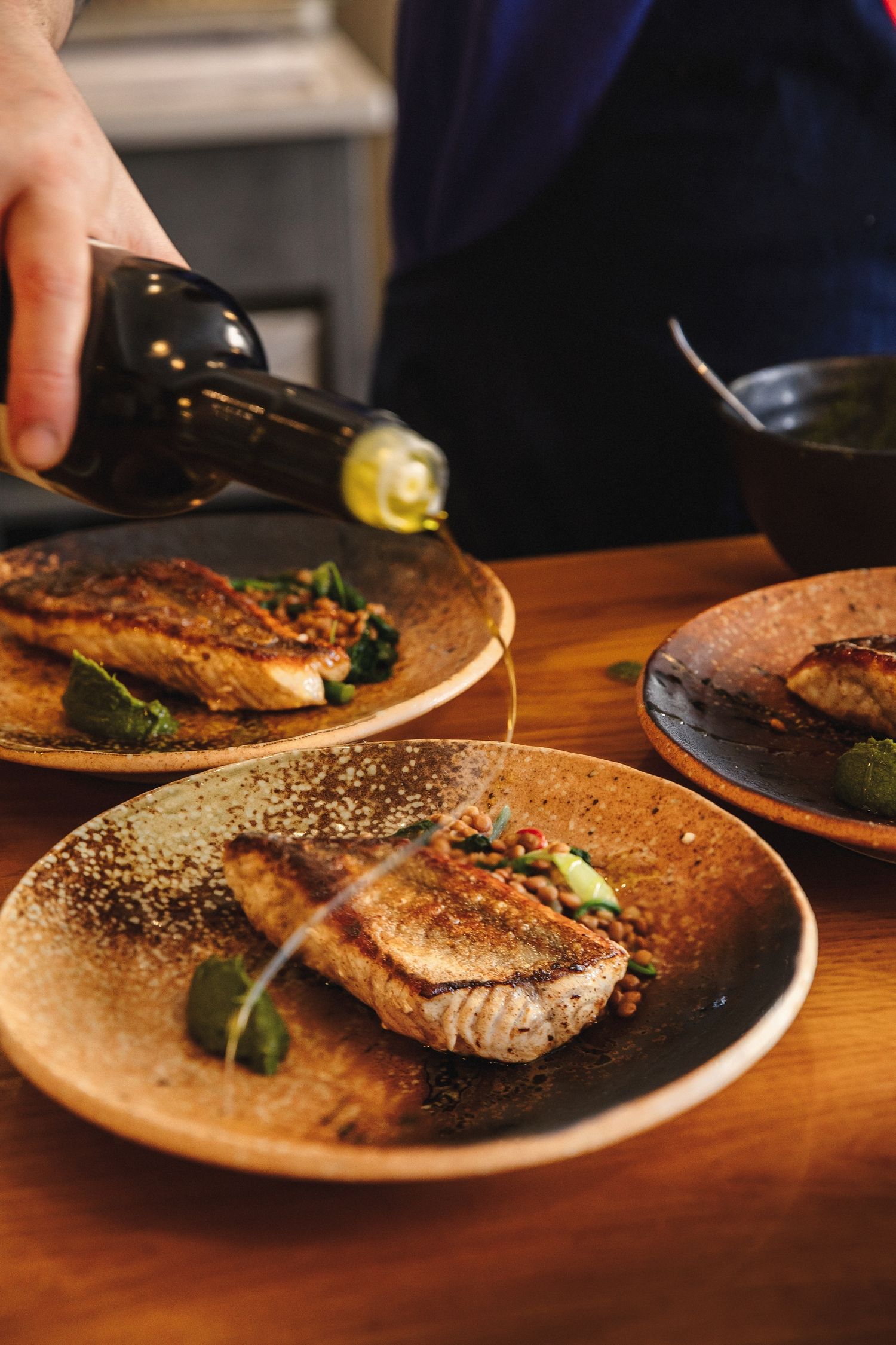 Wine being poured over seared tuna steaks served on rustic brown plates on a wooden table in a restaurant setting.