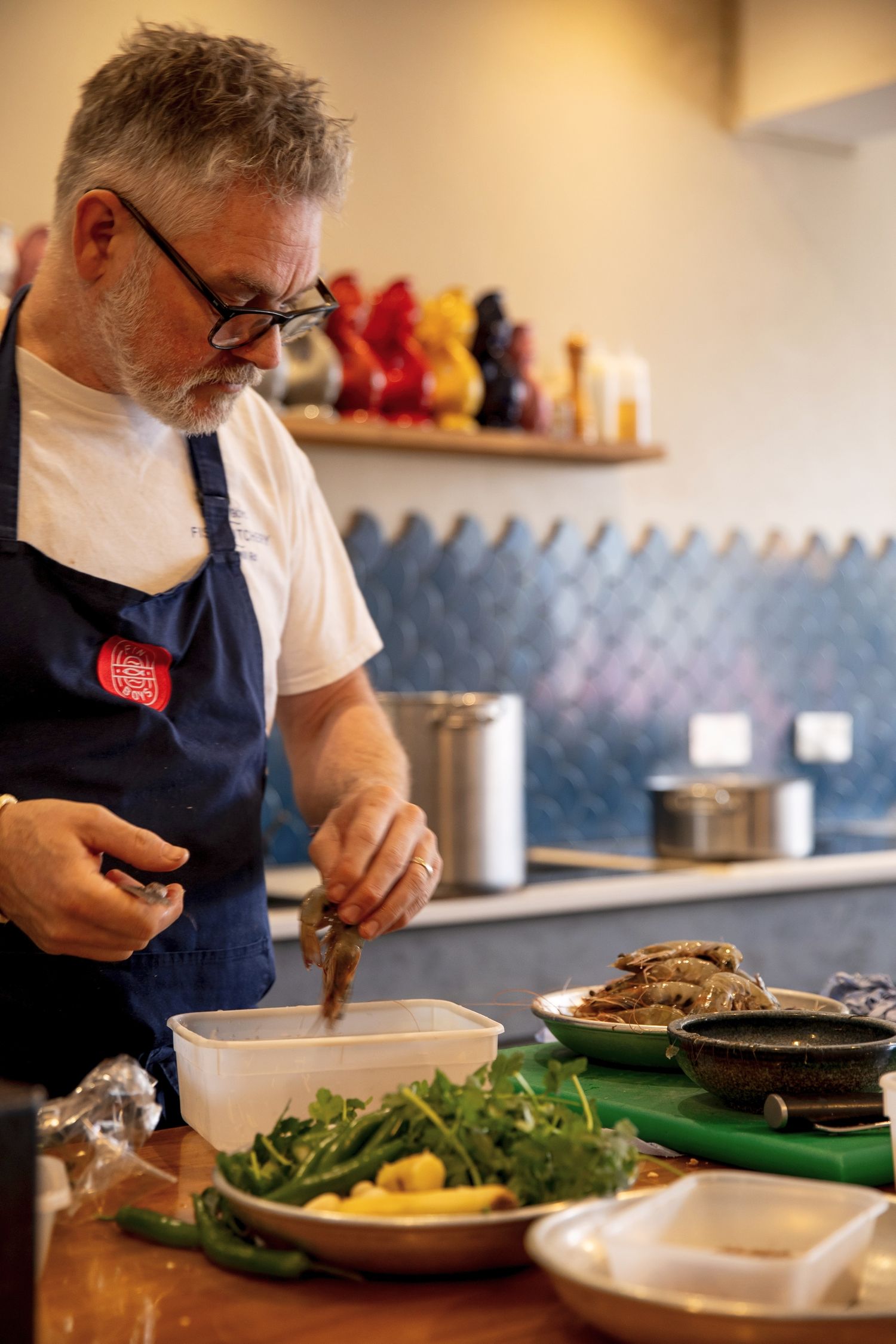 A series of food preparation photos showing someone in a navy apron plating dishes in a restaurant kitchen.