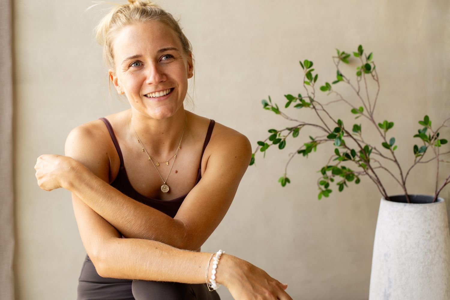 Natural relaxed portrait of a fitness enthusiast again a cream background with elegant plants in the background.