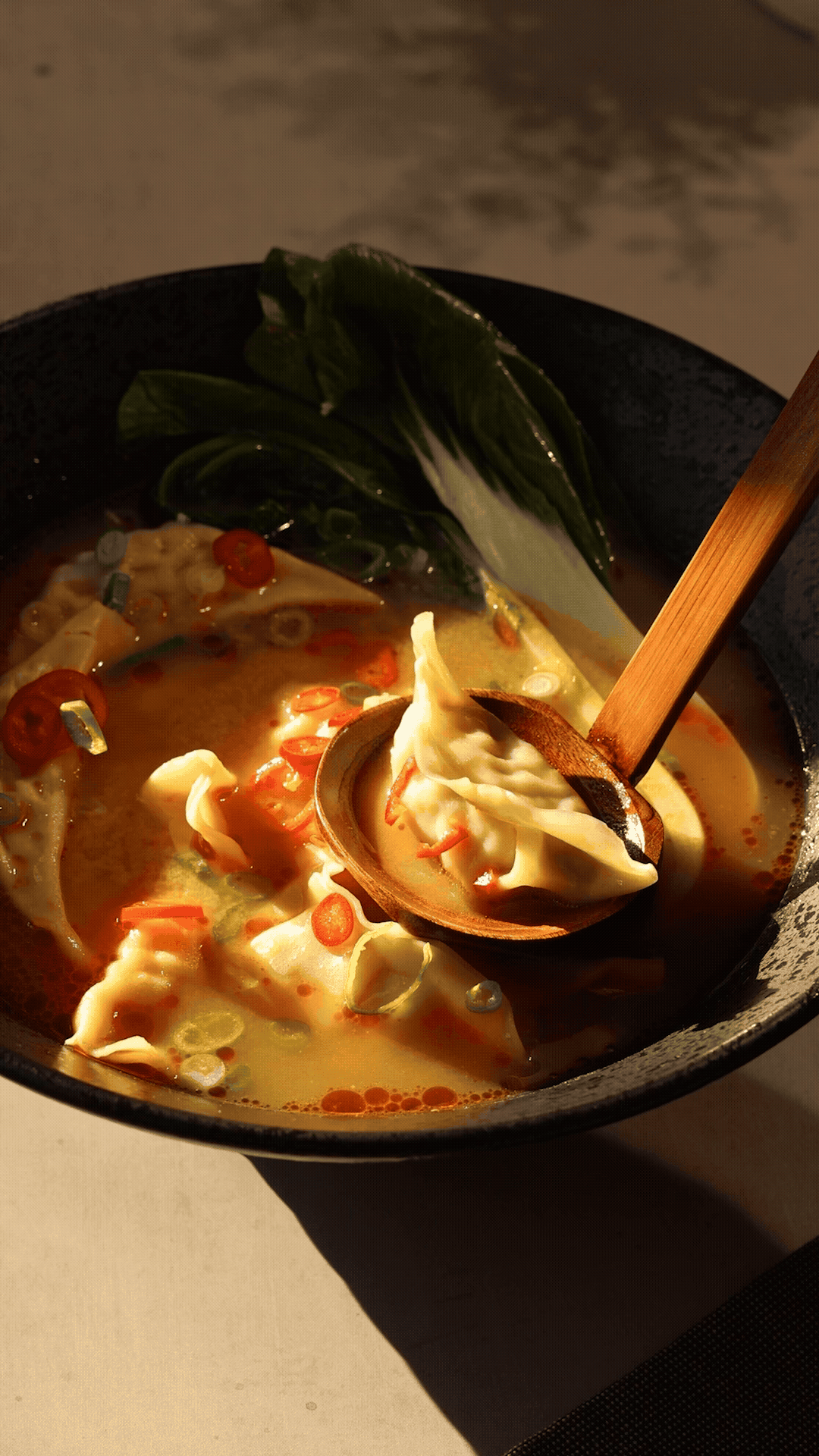 Short video of japanese gyoza soup in large dark bowl in a cosy setting.