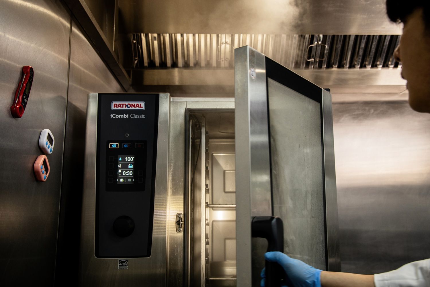 Chef opening a Rational iCombi Classic commercial combi oven in a professional kitchen.