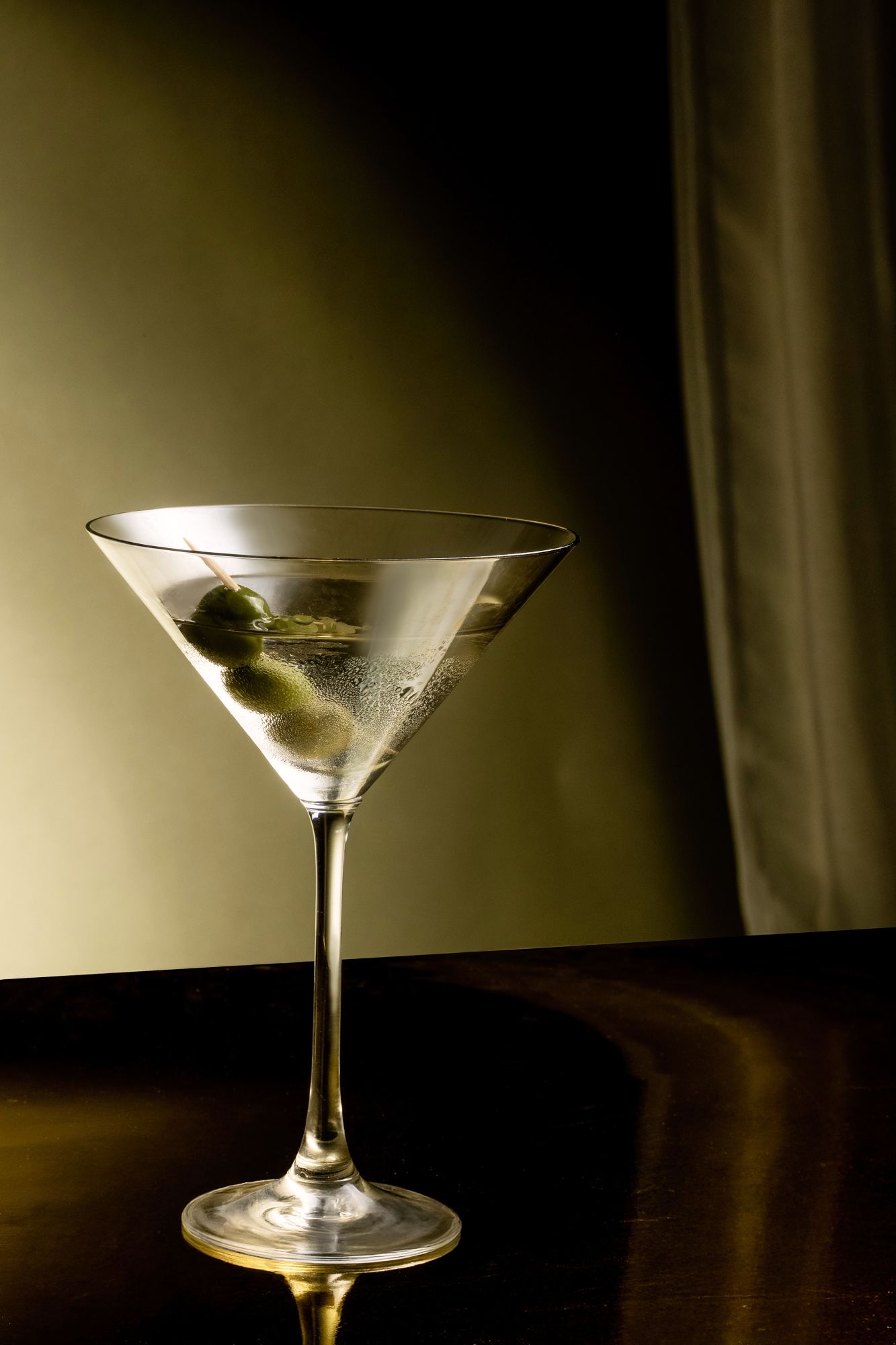 A classic martini glass with olive garnish captured in dramatic low-key lighting against a dark background.