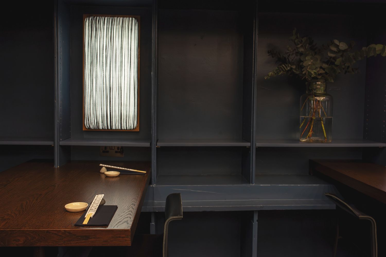A modern office interior with dark walls features a sleek white pendant lamp casting ambient light in the workspace.