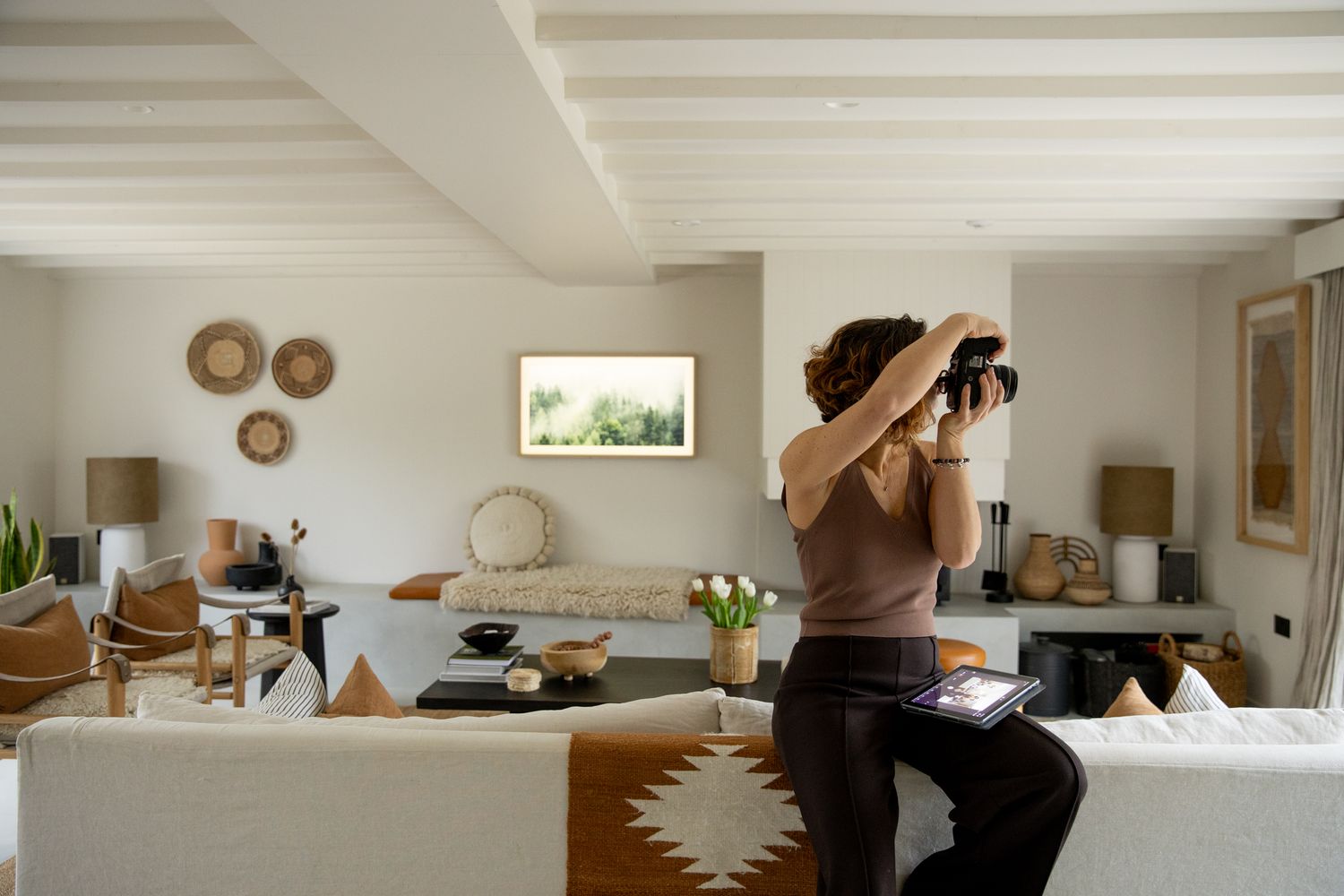 Photographer in modern minimalist living room interior with white walls and wooden furniture.