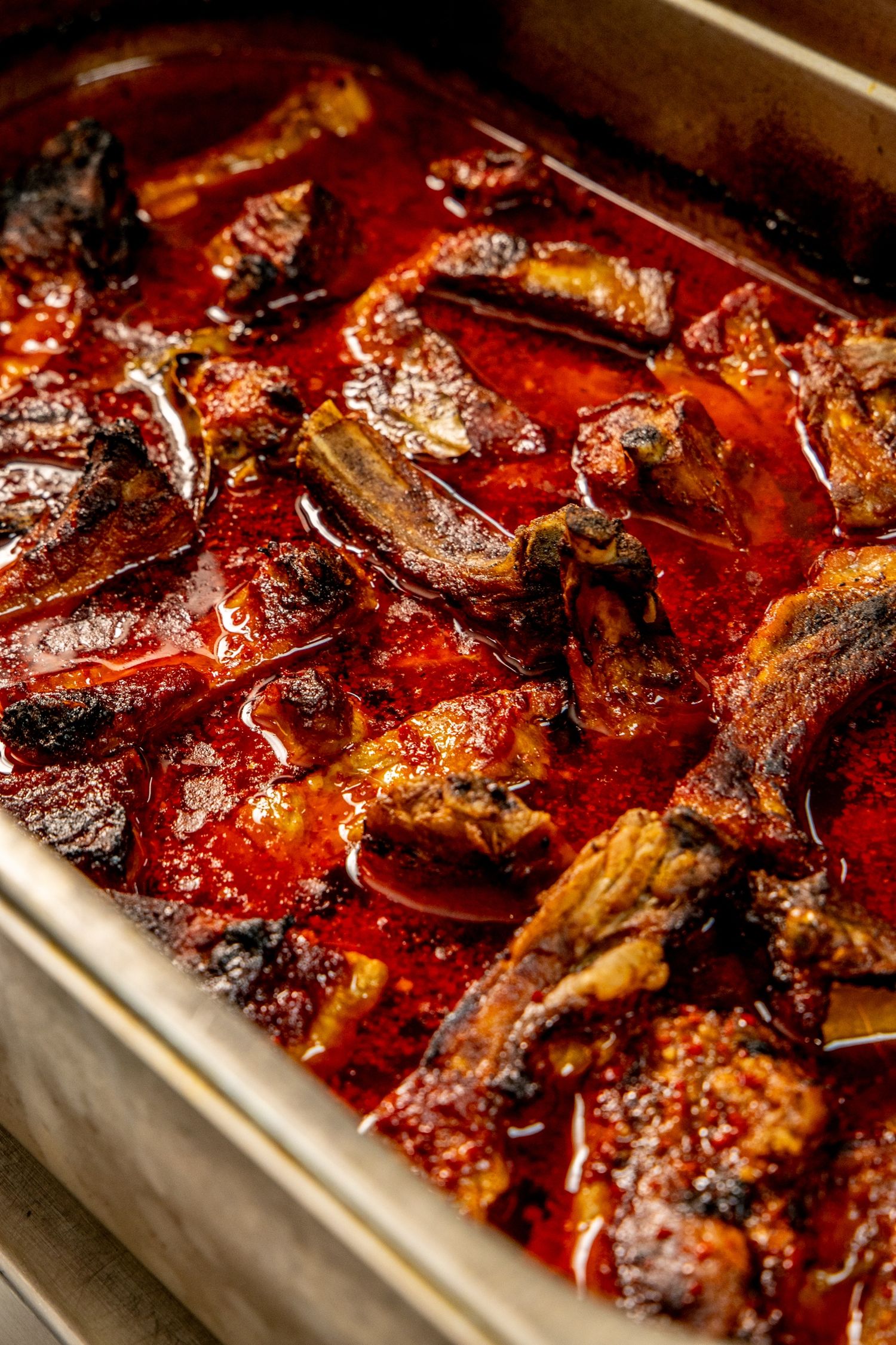 Braised beef short ribs in rich red tomato sauce cooking in a metal roasting pan.