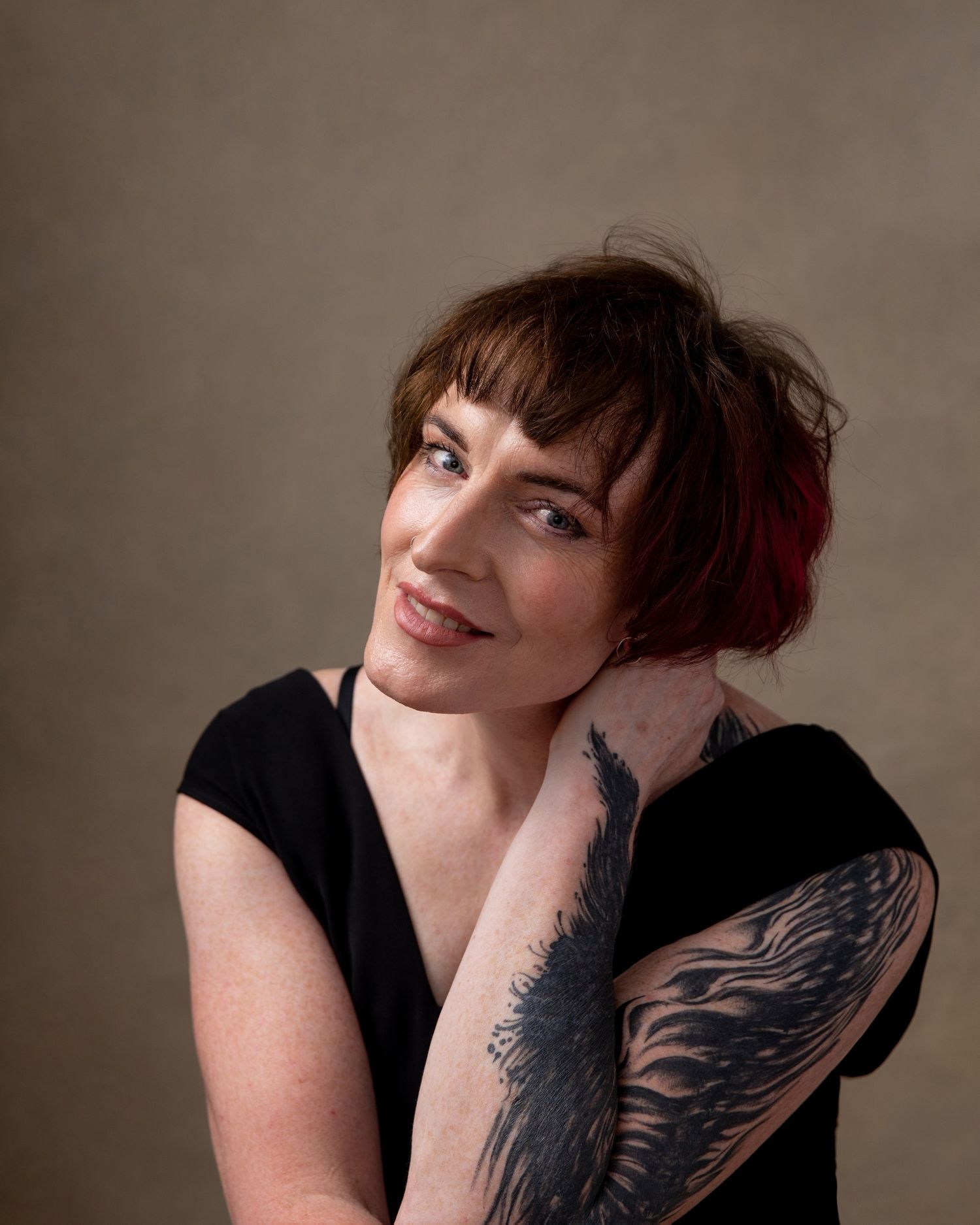 Portrait series showcasing artistic tattoo and black top against neutral background.