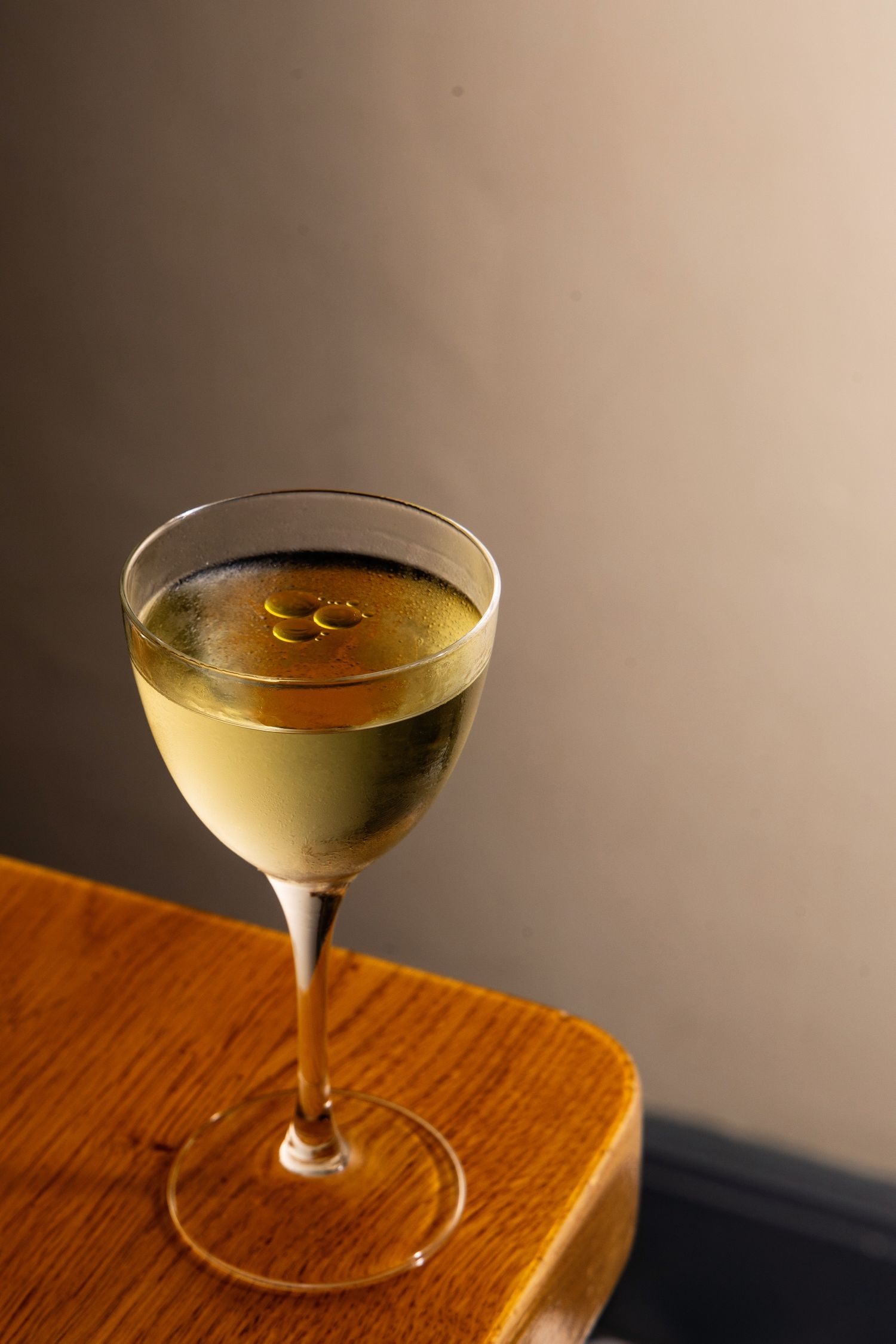 Four elegant coupe glasses filled with golden martini cocktails sit on a wooden surface in moody lighting.