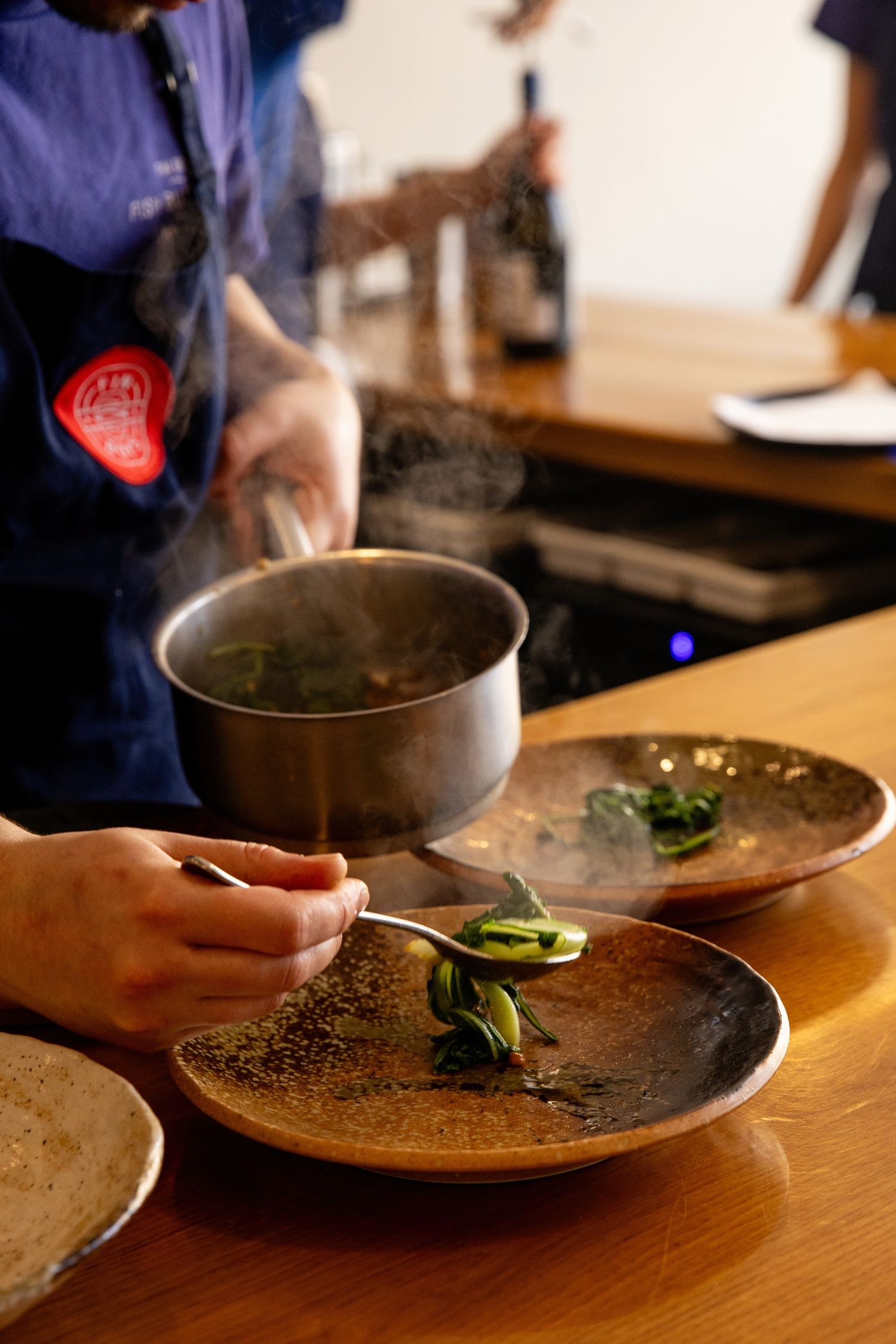 The image shows a person's hands preparing a meal, with a bowl of steaming liquid and a plate of food on a wooden table.