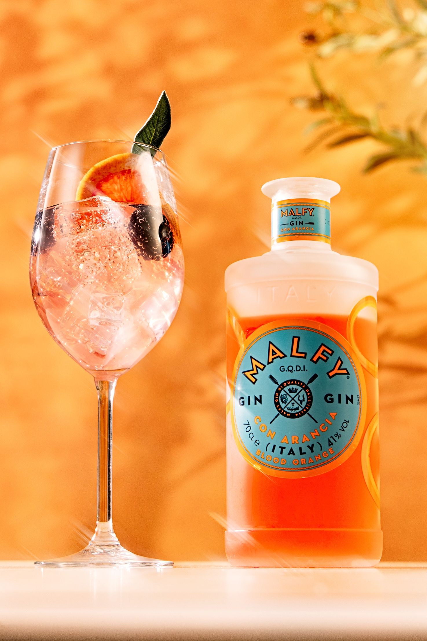 A series of pink cocktails in coupe glasses with Malfy gin bottles displayed against a warm orange background.