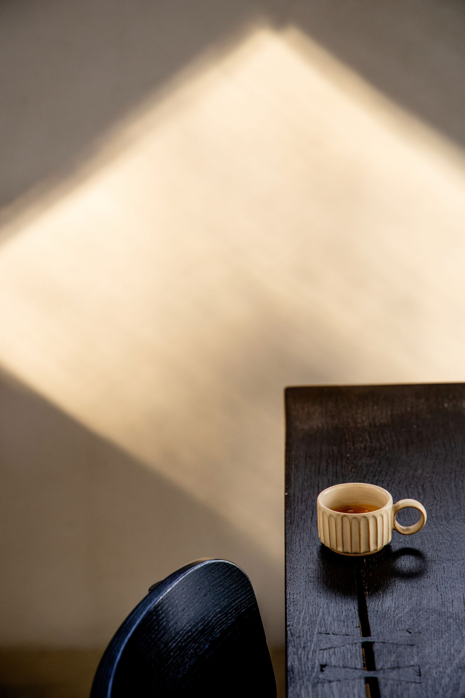 Coffee cup casting dramatic shadows on a dark wooden table in moody lighting.