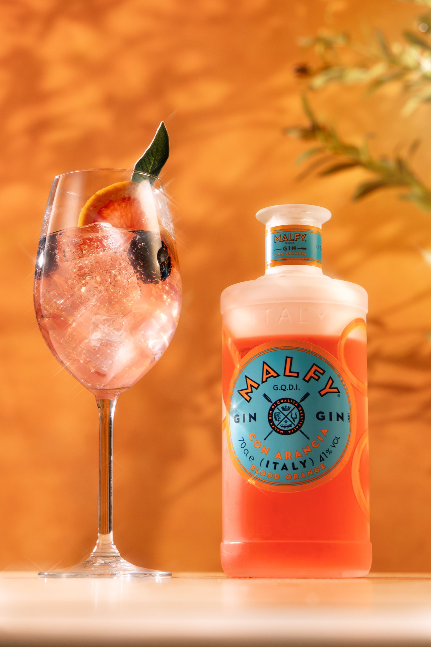 Malfy Con Arancia blood orange gin bottle beside a garnished gin and tonic cocktail on an orange background.