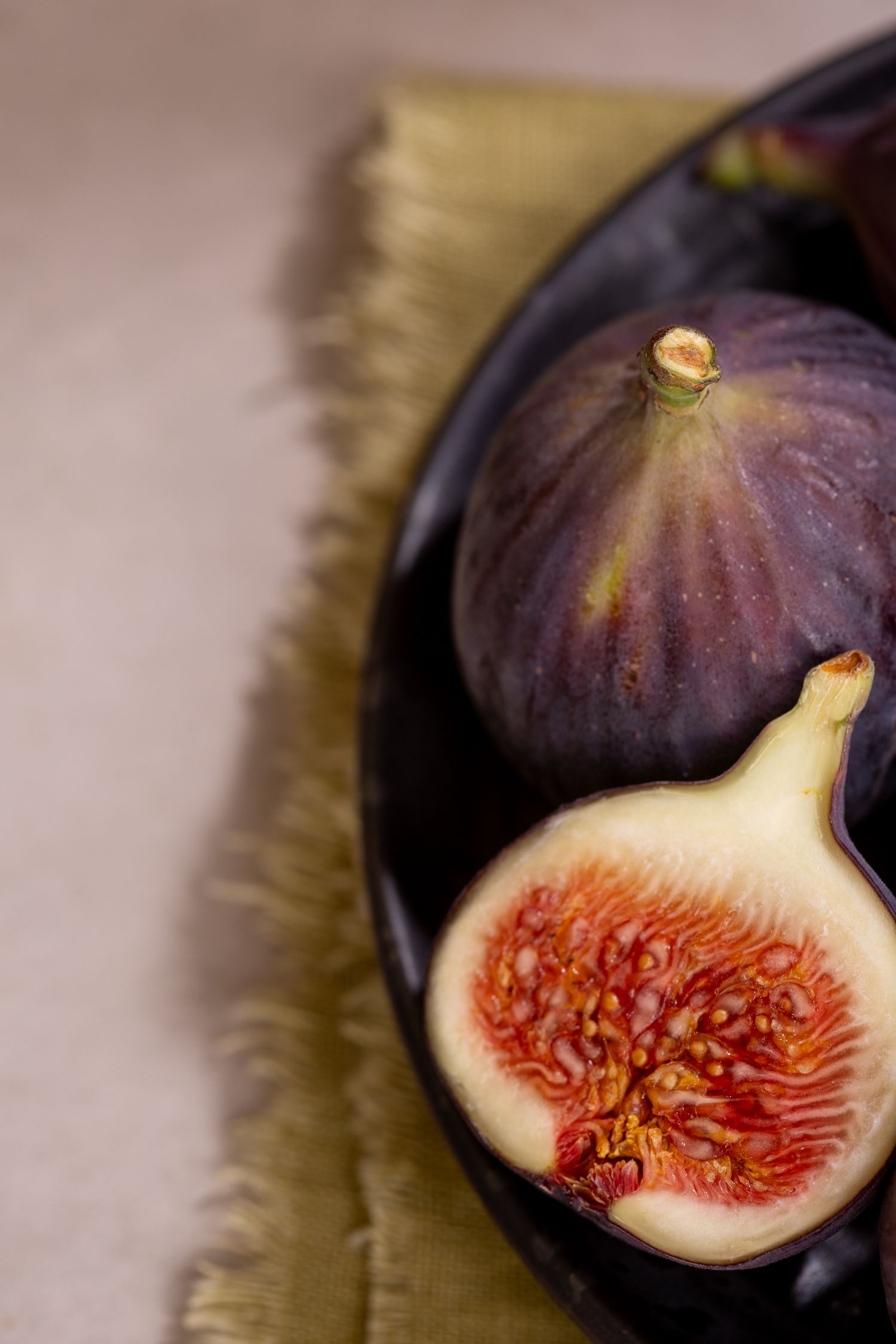 Fresh purple figs on a dark plate, one sliced open revealing red flesh, placed on a green linen napkin.