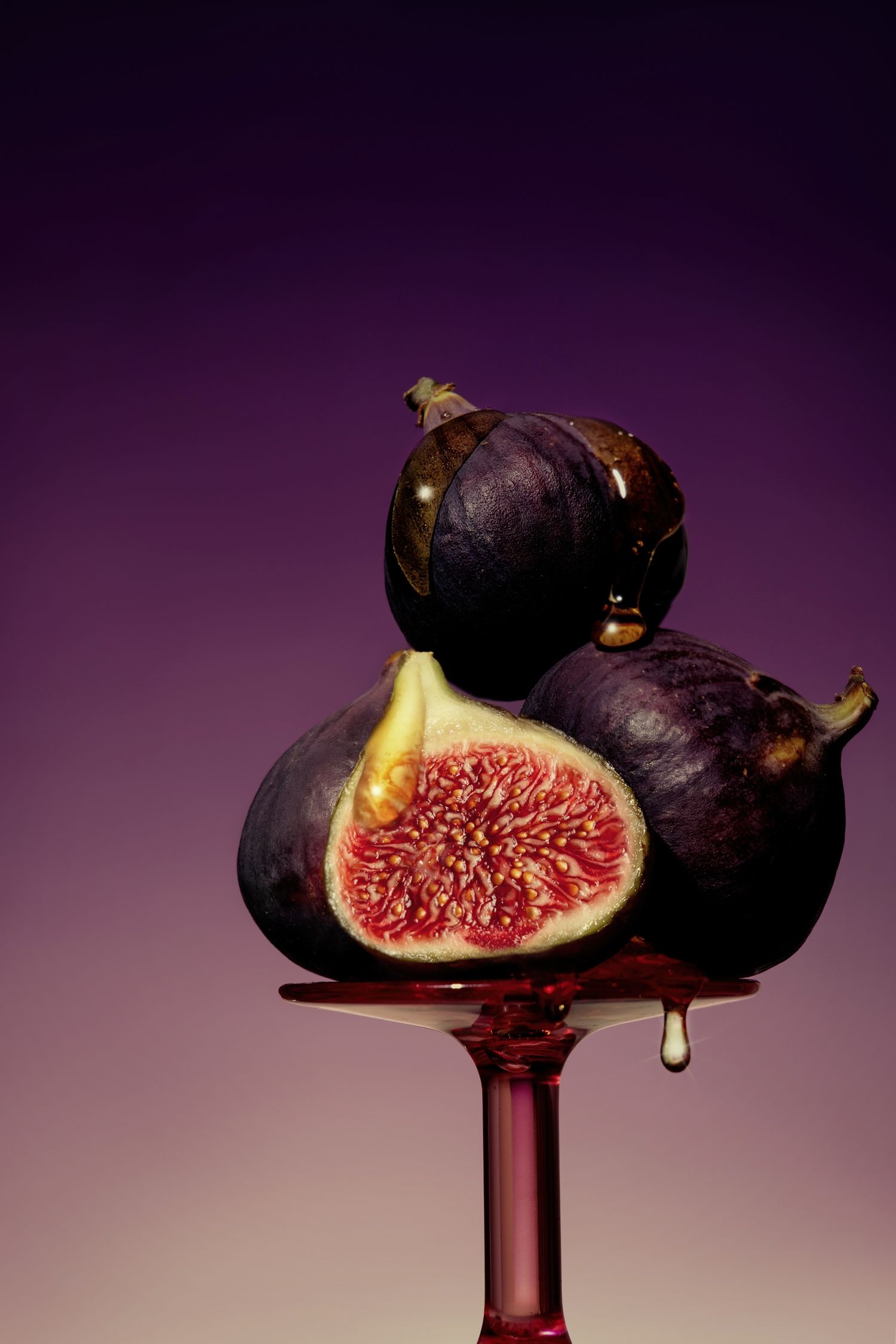 Artistic still life of sliced figs on dark purple background with dramatic lighting and honey drip.