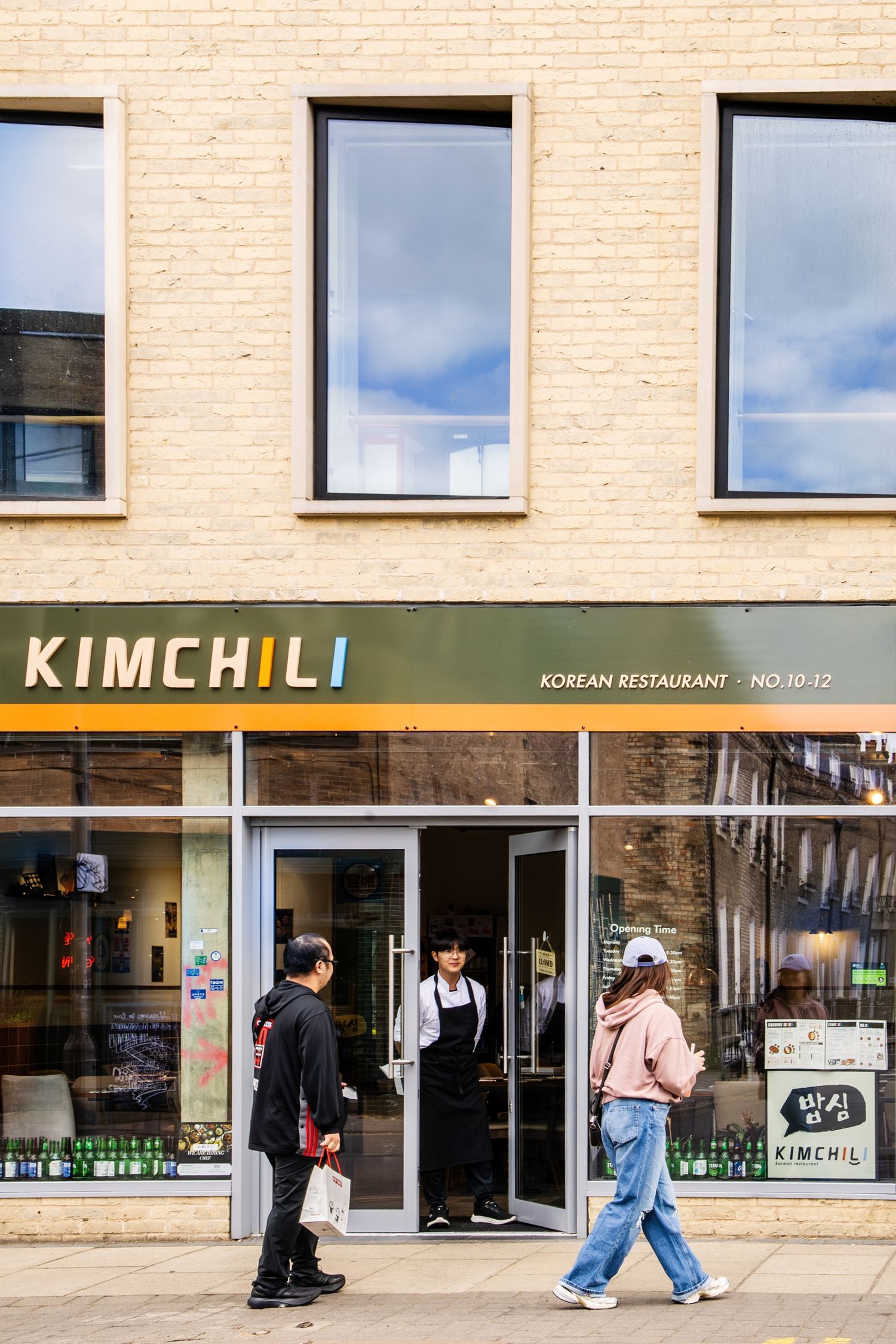 People walking past Kimchili Korean Restaurant storefront at No. 10-12, featuring a green and yellow sign.