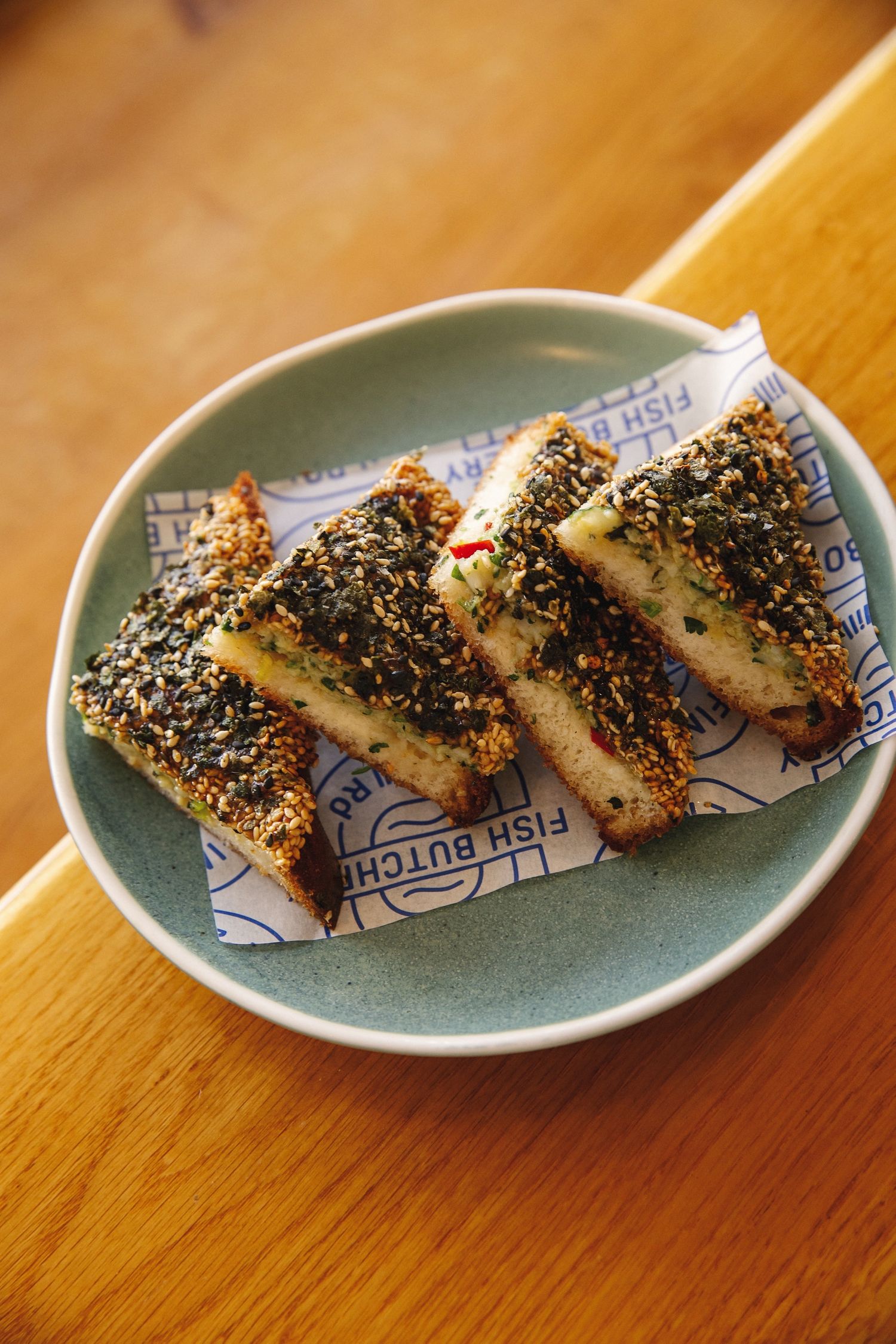 Sushi rolls coated in black sesame seeds arranged on a blue ceramic plate sitting on a wooden table.