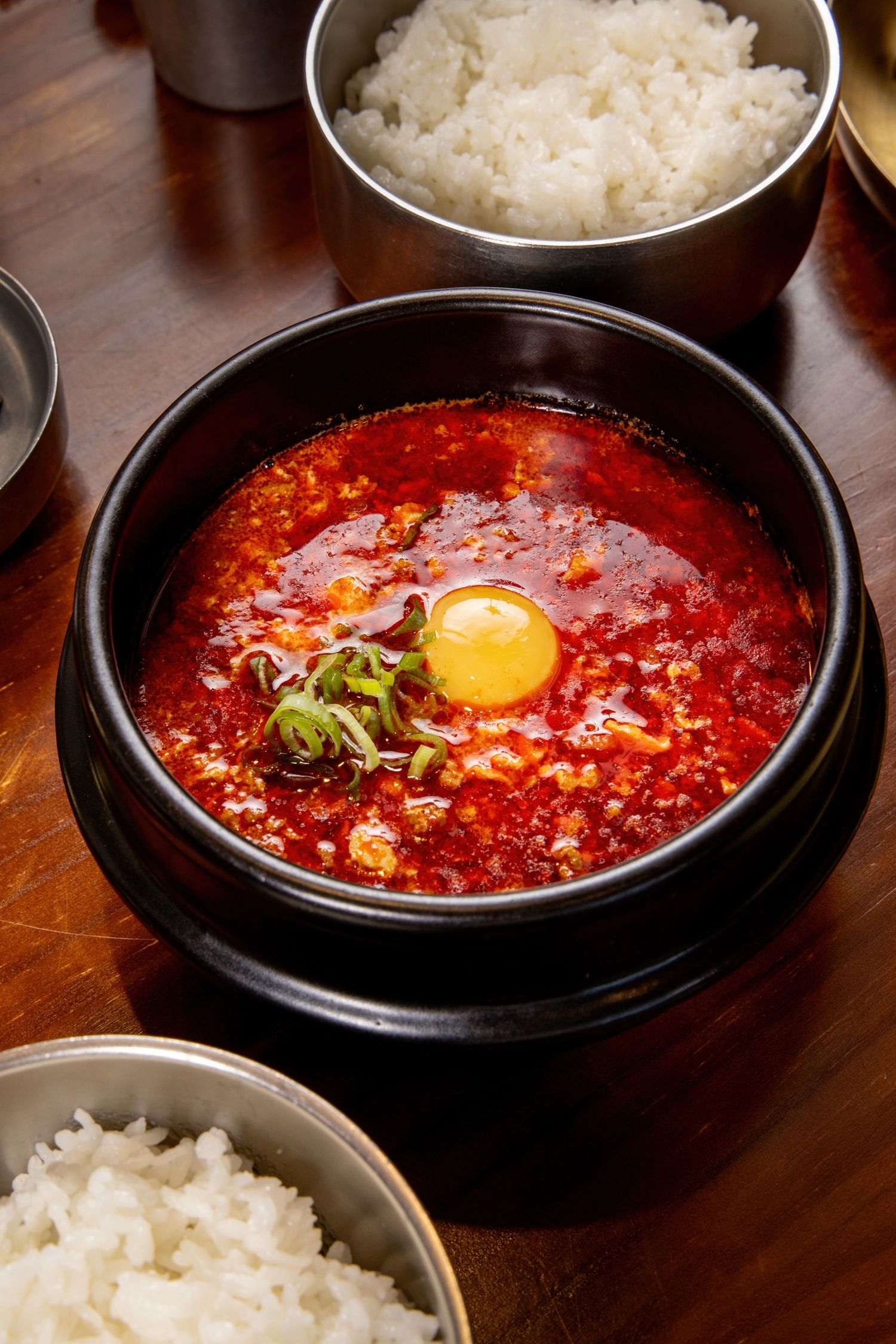 Spicy Korean sundubu jjigae tofu stew with egg yolk in black stone bowl served with steamed white rice.