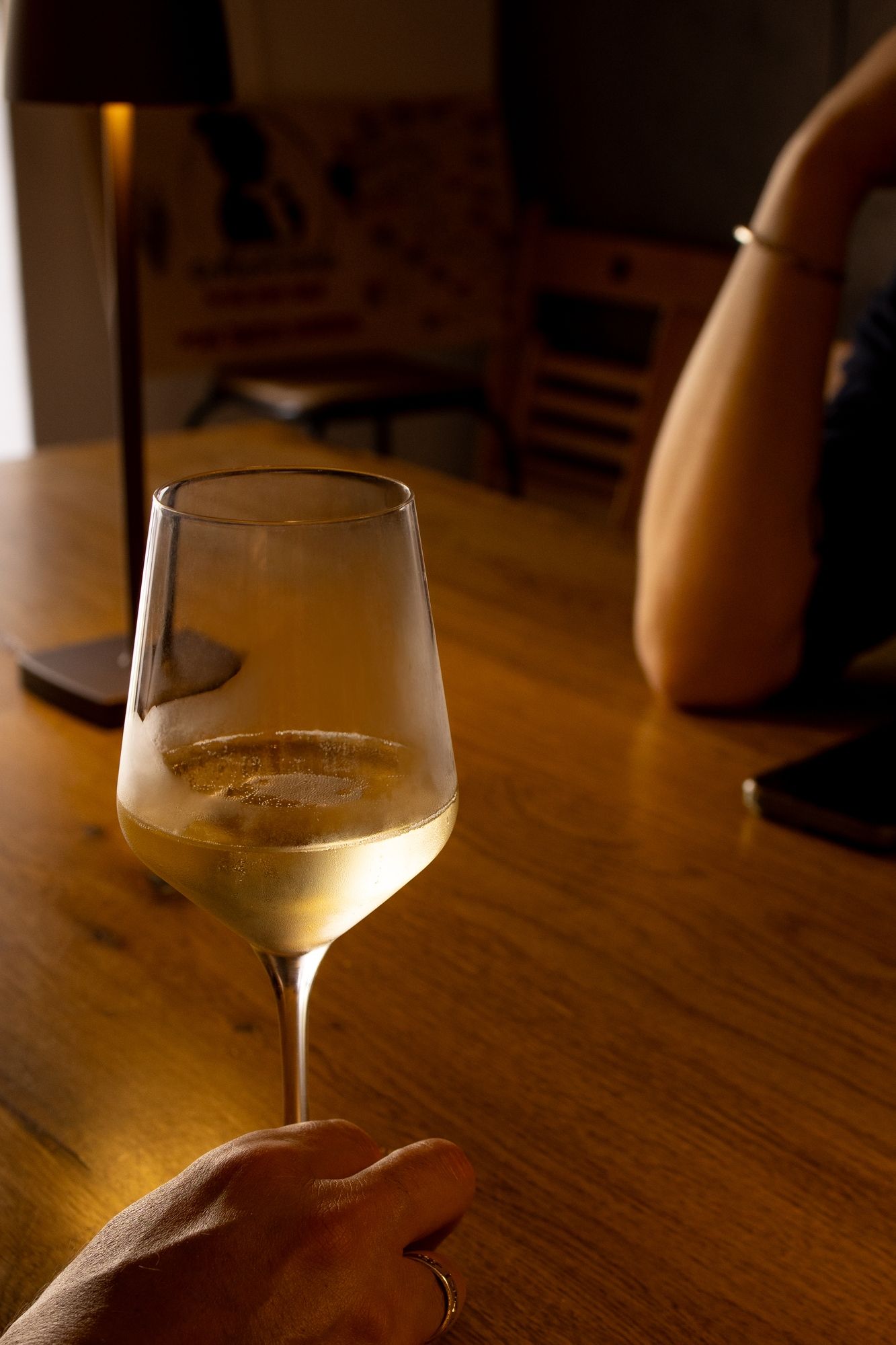 Glass of white wine on wooden table in warm ambient lighting.