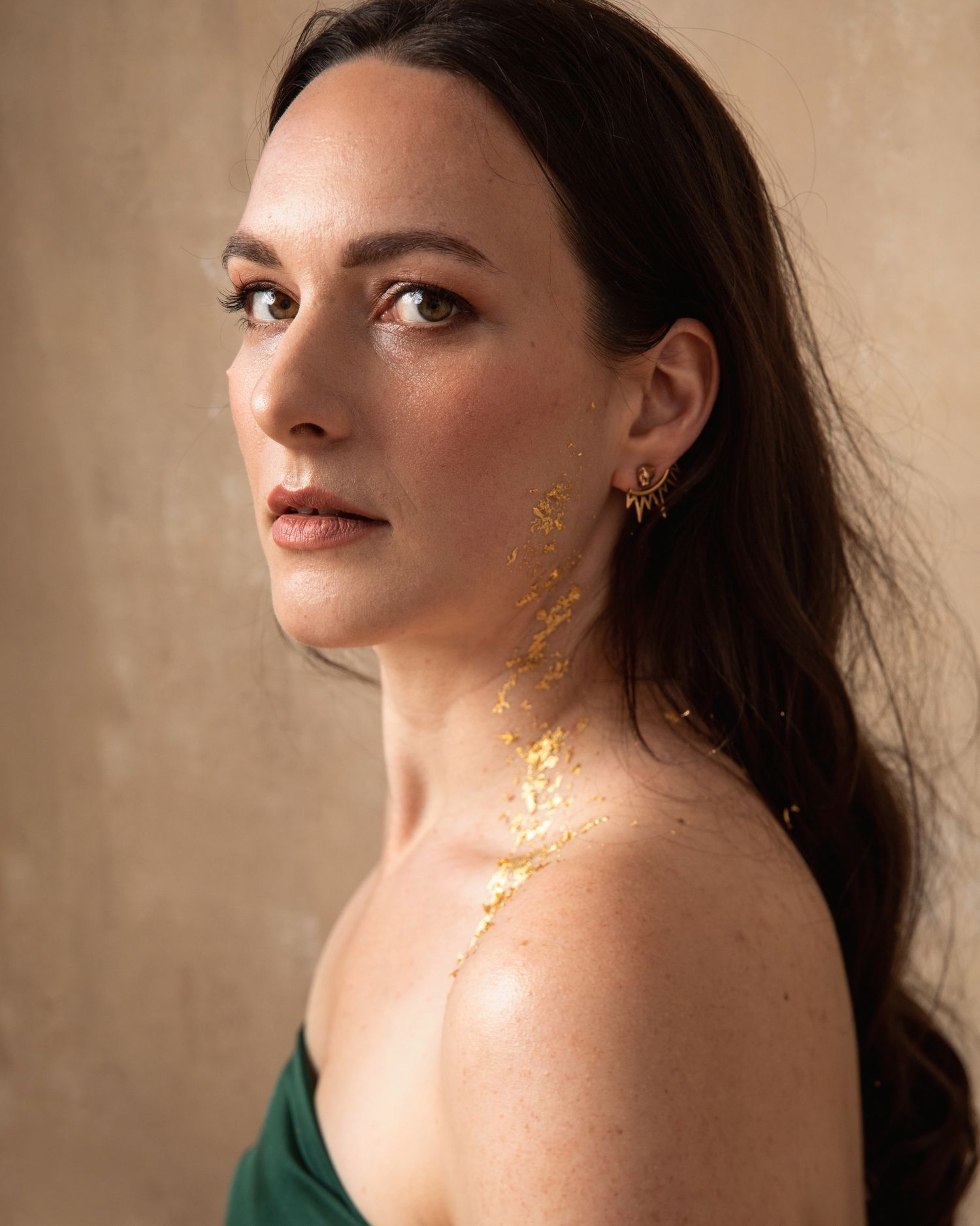 Artistic portrait with gold leaf details applied to skin against neutral background.