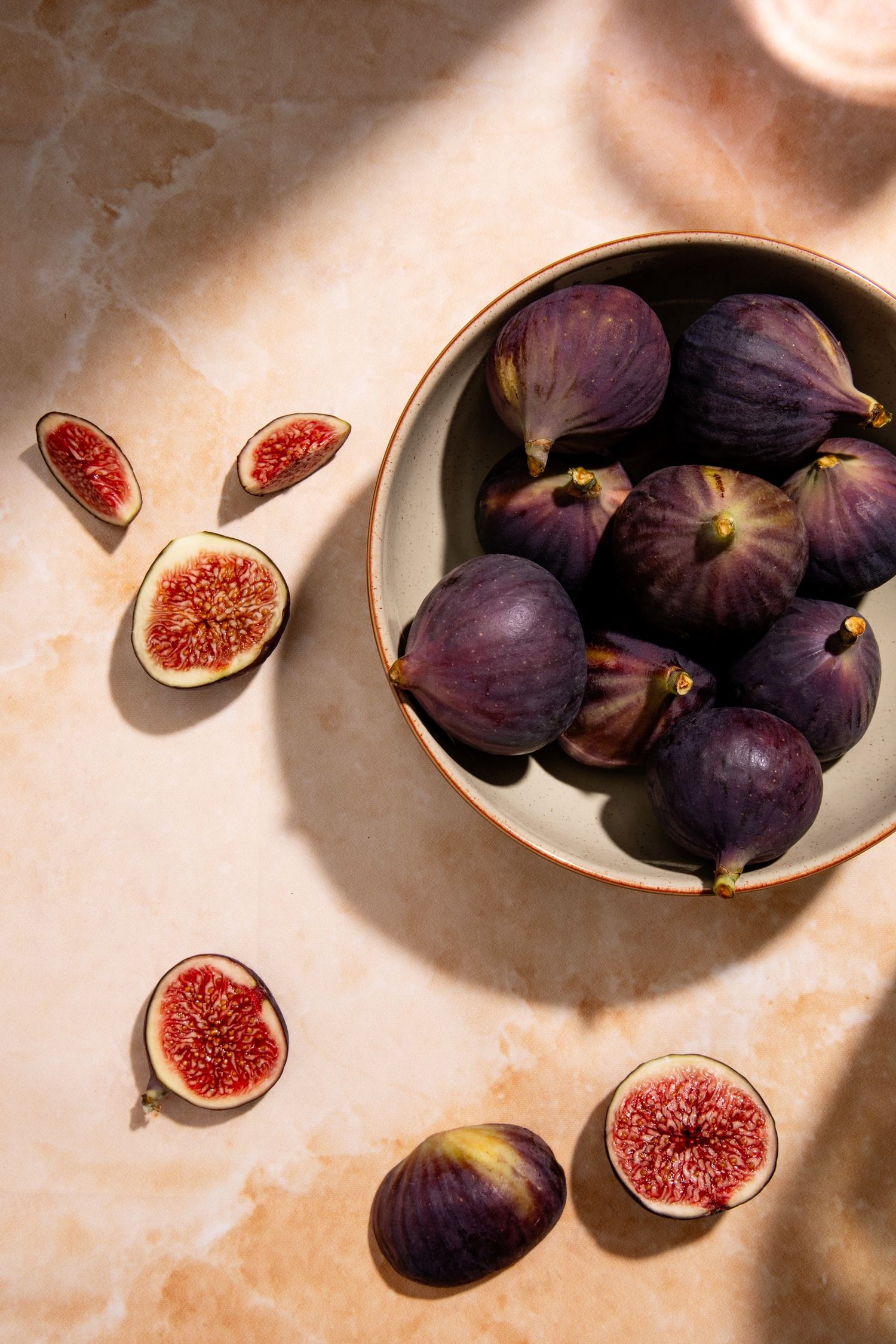 Fresh purple figs arranged on ceramic bowl with sliced cross-sections showing red interior. Warmly lit with a late summer feeling.
