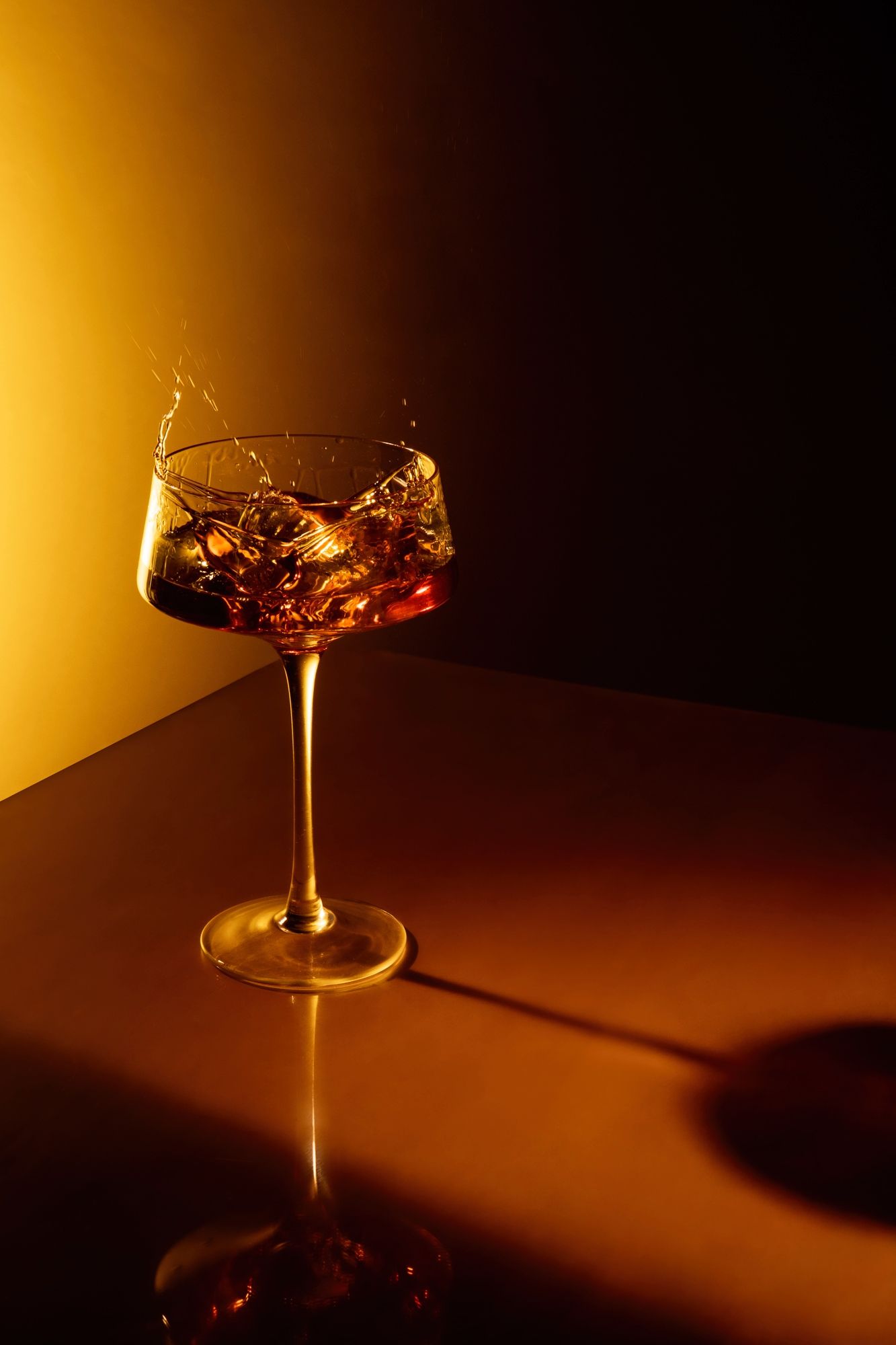 Wine glass filled with amber liquid captured in dramatic golden lighting against dark background.