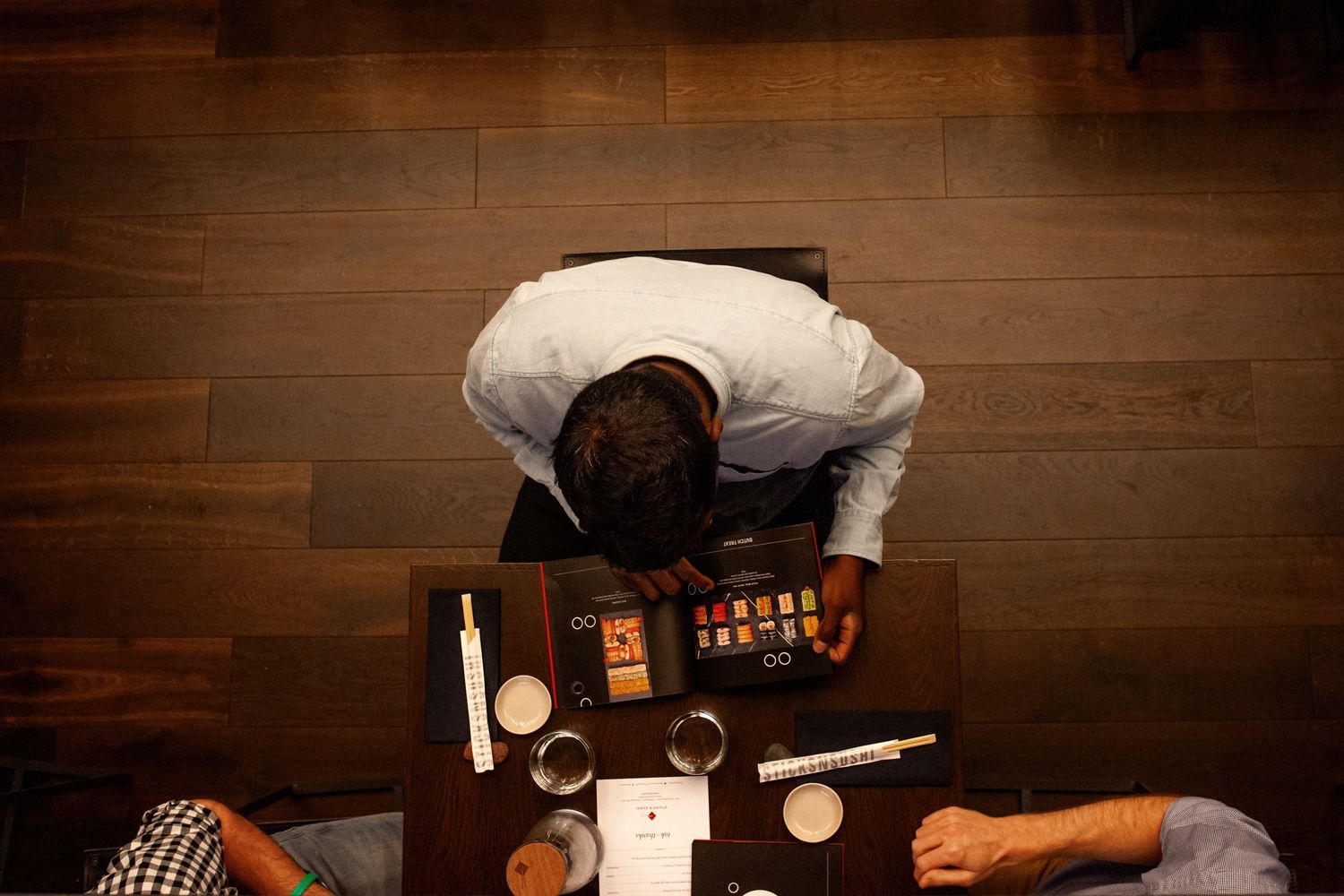 A bartender demonstrates cocktail making techniques at a wooden bar counter with bottles and glassware.