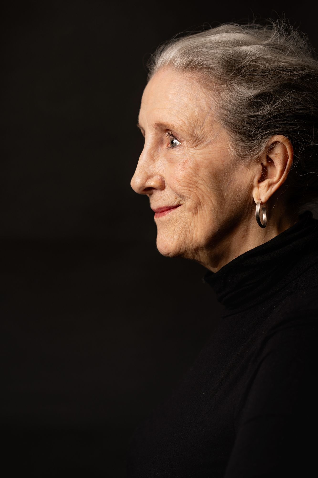 Elegant profile portrait of a senior woman in black turtleneck against dark background.