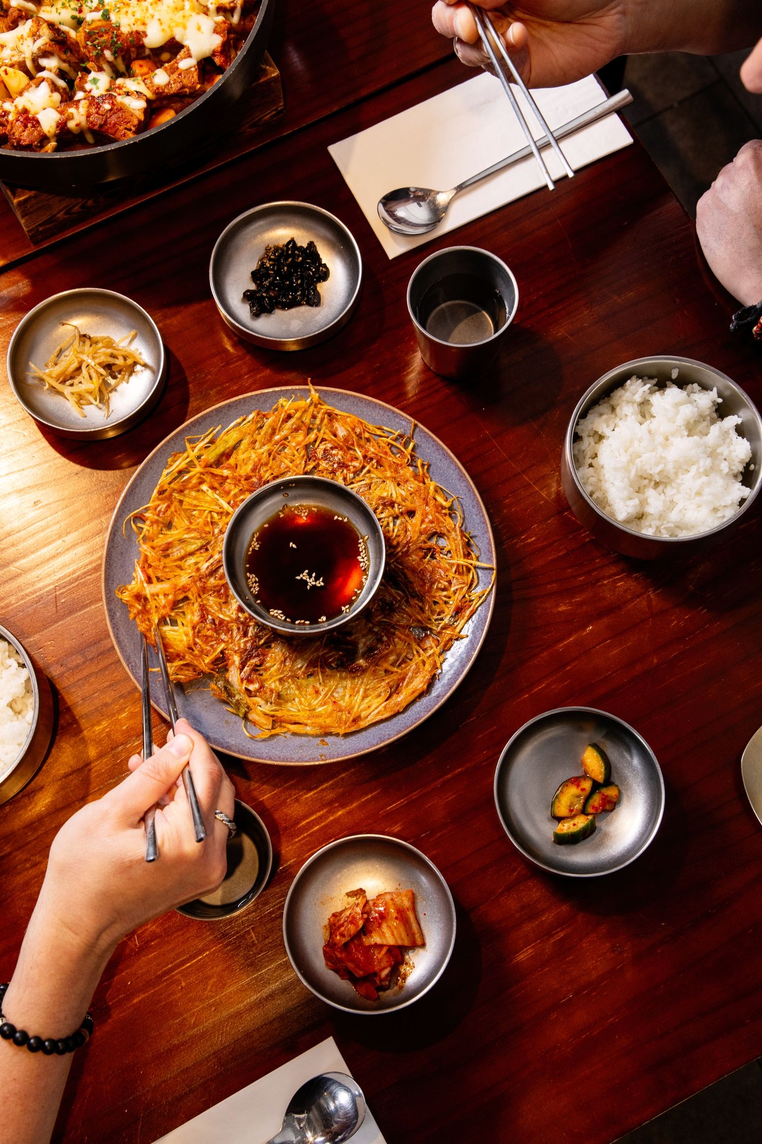 Korean dining table with crispy hash brown dish, dipping sauce, rice, kimchi, and assorted banchan side dishes.