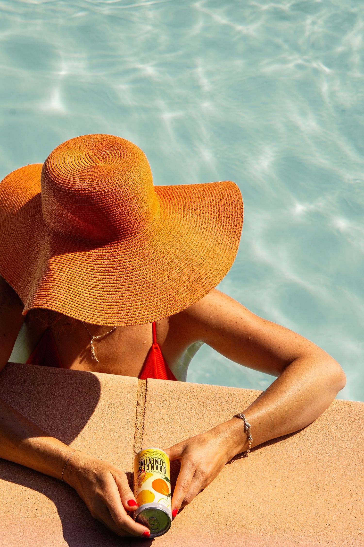Orange sun hat and relaxing poolside scene with turquoise water reflections.