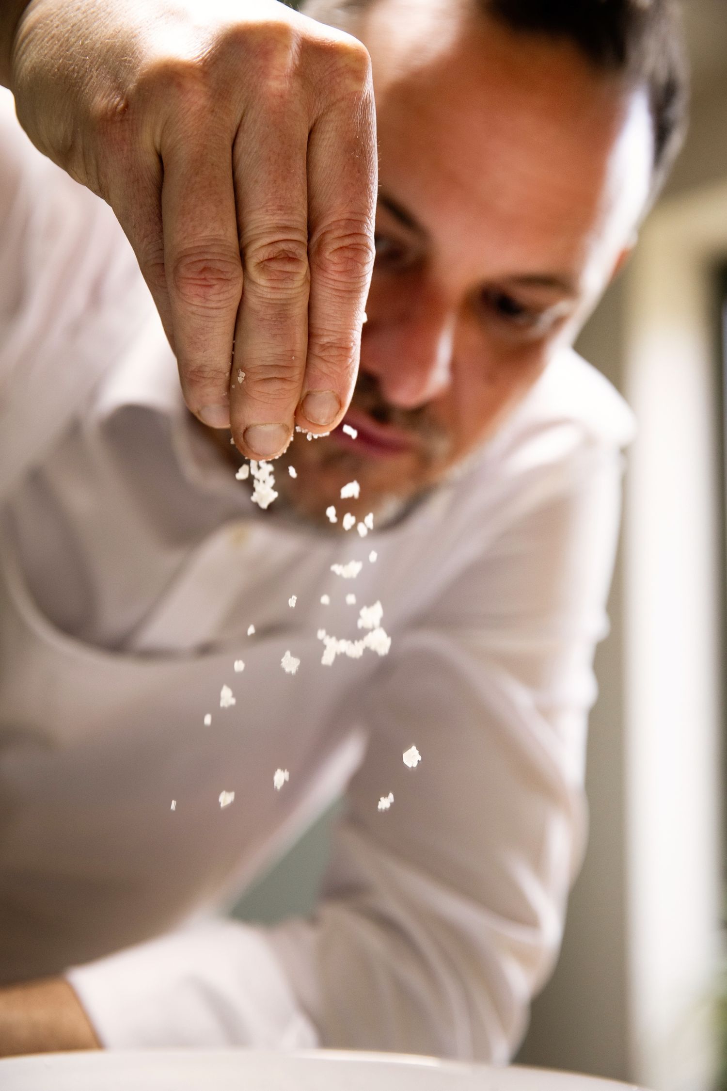 Chef sprinkles salt with fingers in a professional kitchen in a sequence of close-up shots.