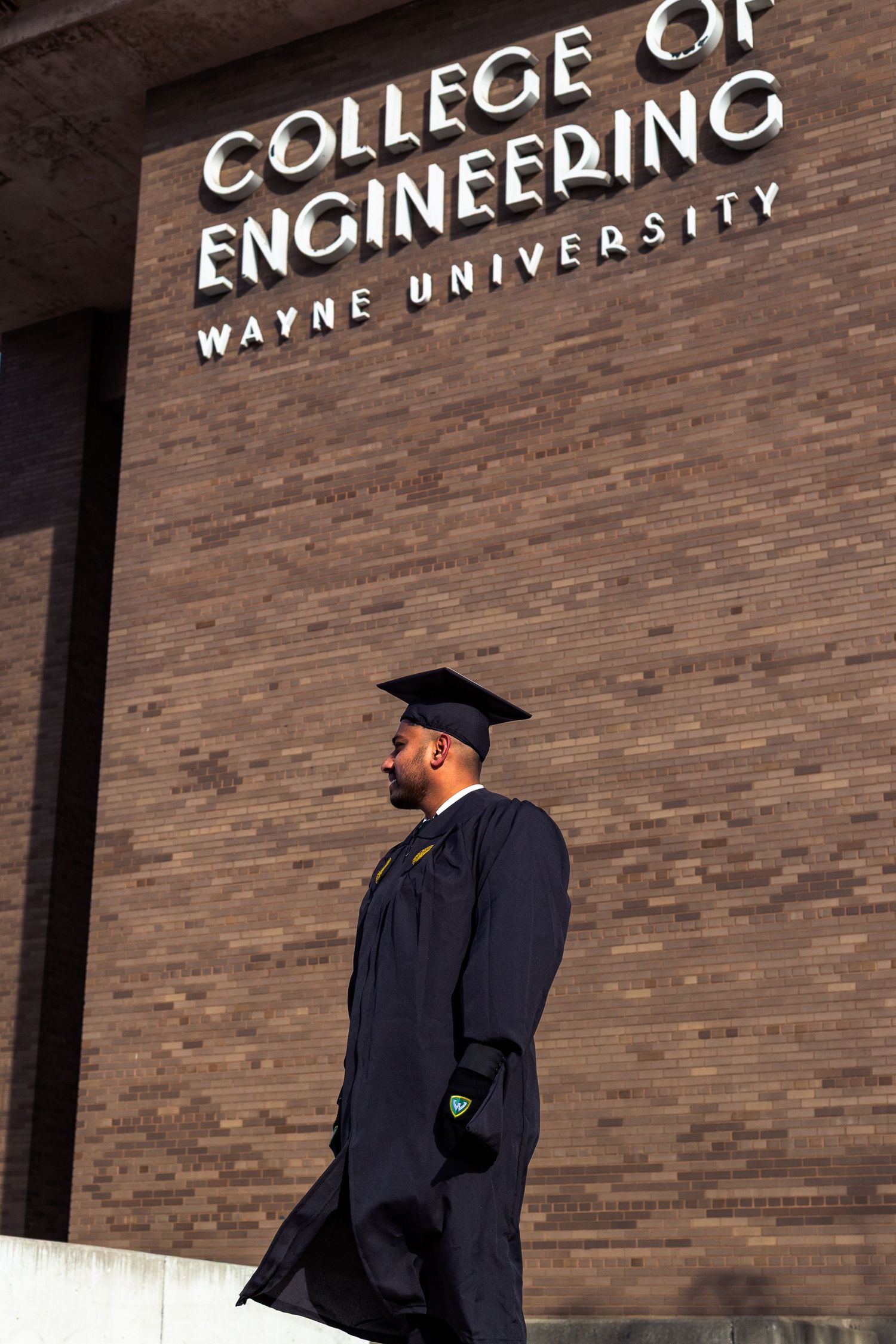 Wayne State College of Engineering graduate in cap and gown stands before brick building.