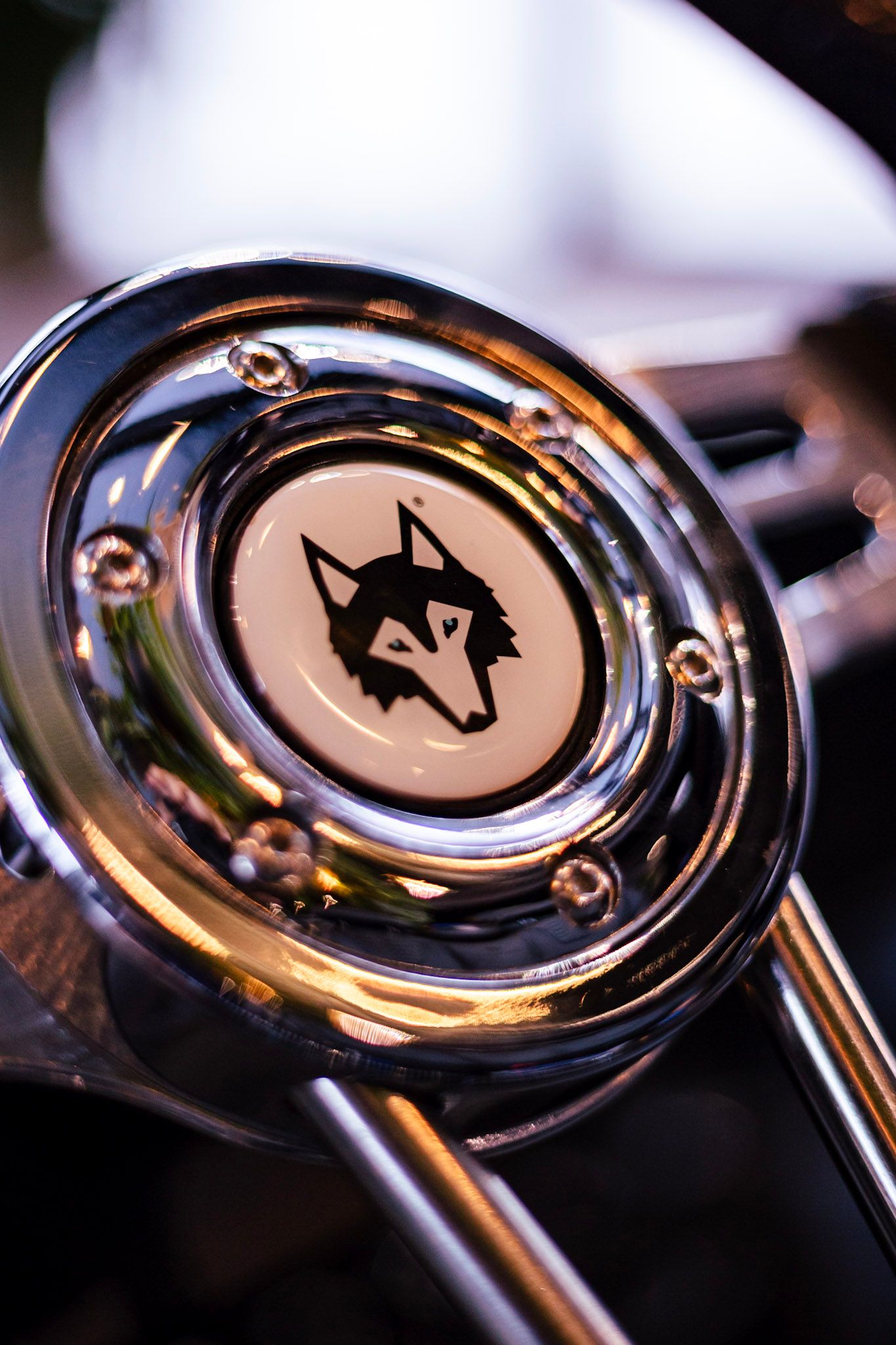Close-up of a chrome steering wheel horn button featuring a black wolf head logo emblem.