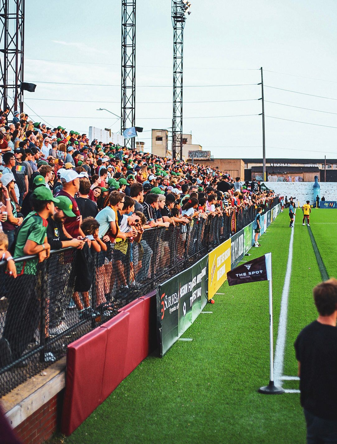 A large crowd of Detroit City FC fans in green line the fence at Keyworth Stadium during a soccer match.