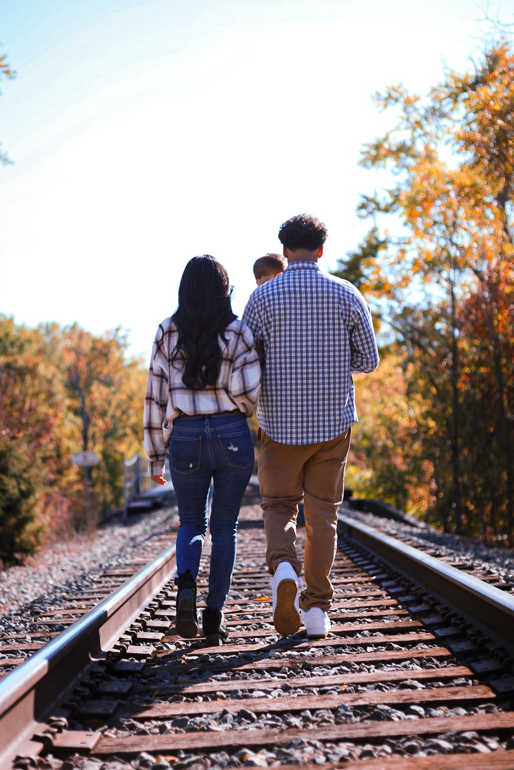 A couple walks hand-in-hand down railroad tracks lined with vibrant fall foliage.