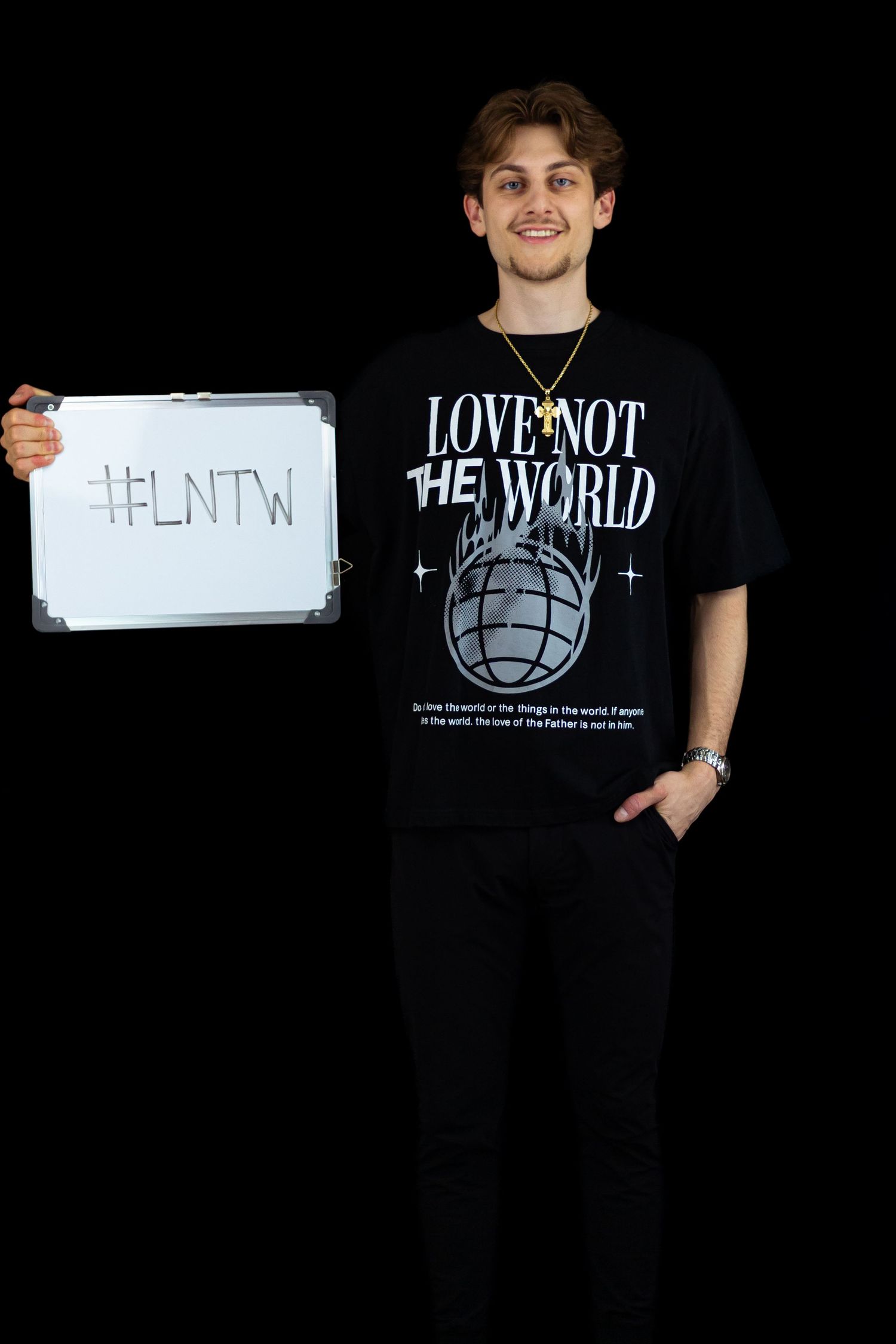 Smiling young man holding whiteboard with #LNTW wearing black Love Not The World graphic t-shirt.