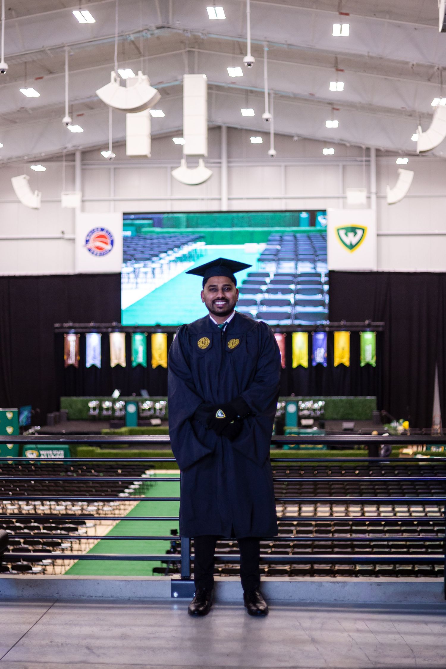 Wayne State University graduate smiling in cap and gown inside graduation ceremony venue.