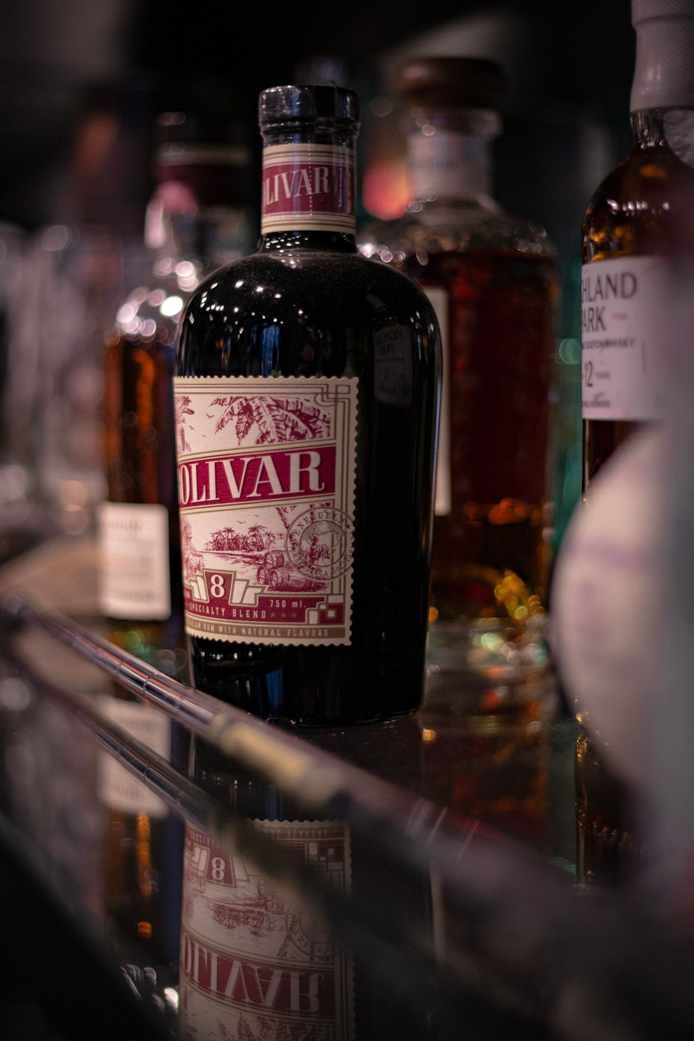 Bottle of Olivar 8 rum on a reflective bar shelf surrounded by other spirits including Highland Park.