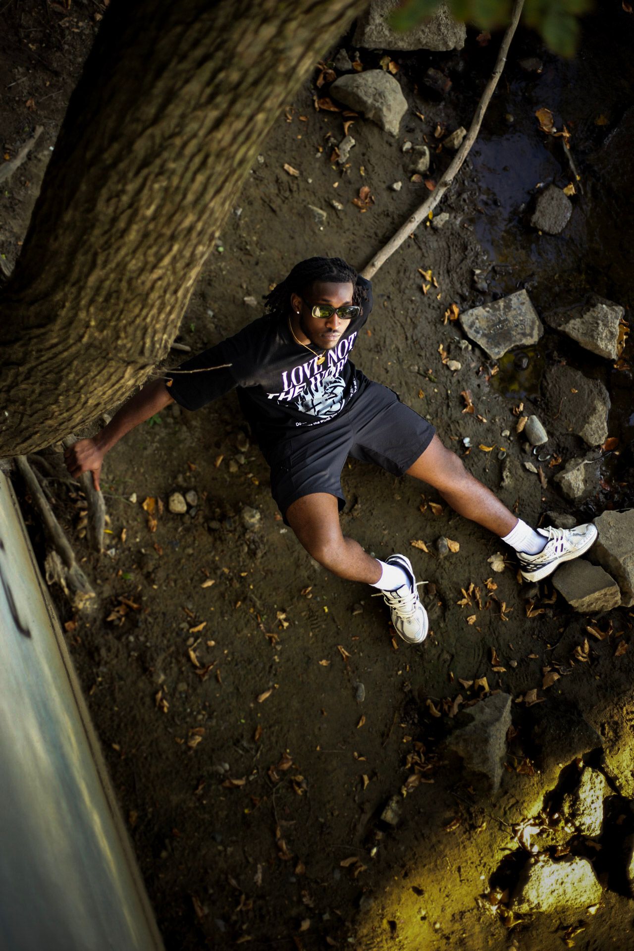 Person leaning against a tree wearing a black graphic t-shirt, photographed from above outdoors.