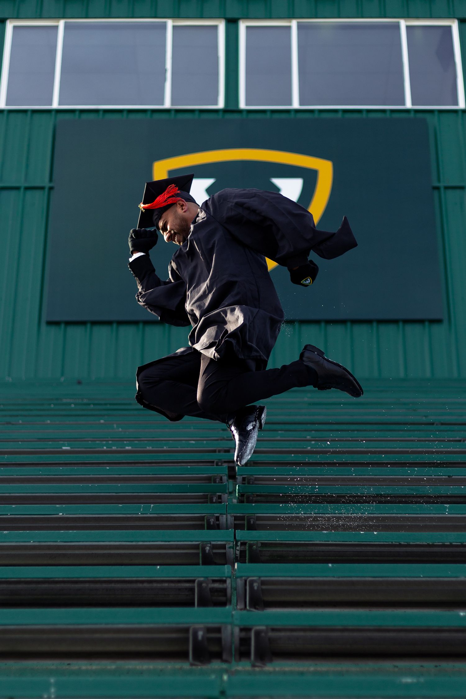 Jubilant Wayne State University graduate leaps in the air in black cap and gown at stadium.