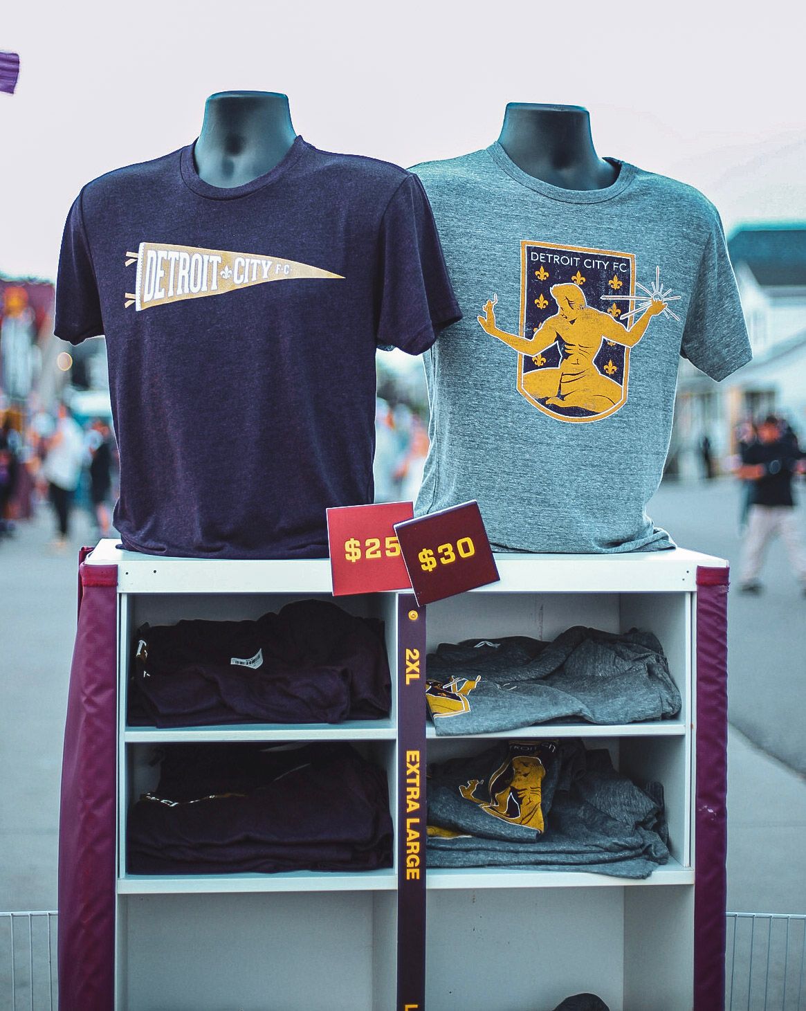 Two Detroit City FC t-shirts on mannequins displayed at an outdoor merchandise stand priced $25 and $30.
