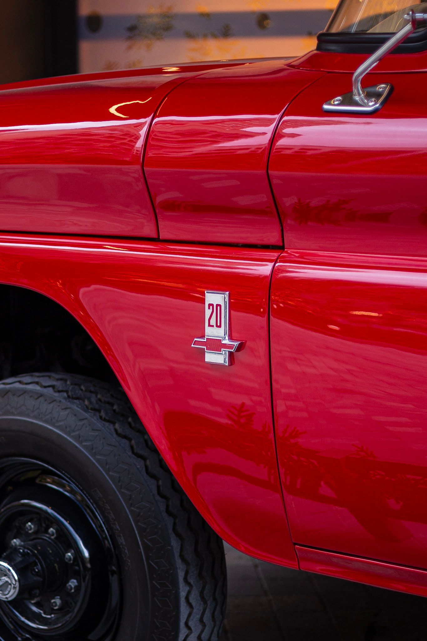 Close-up detail of a red vintage Chevrolet C20 truck badge on a shiny red door panel.