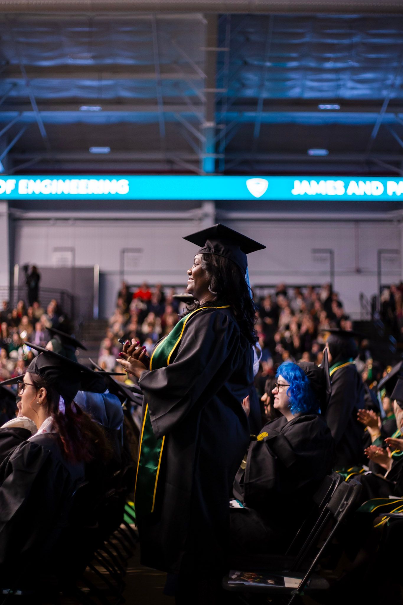 Female graduate in cap and gown stands applauding during Wayne State University graduation ceremony.