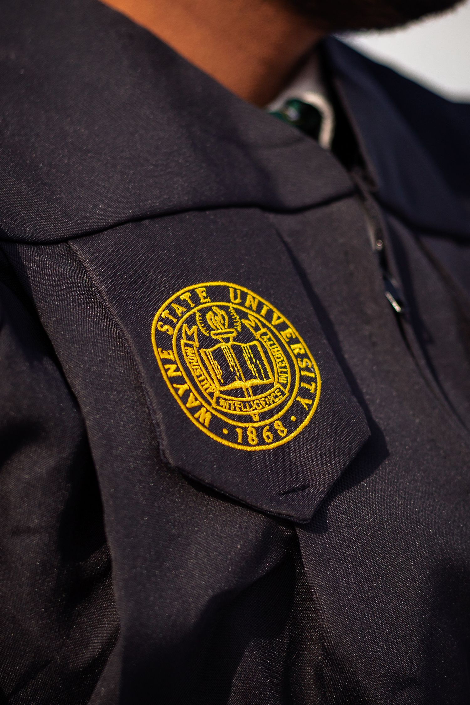 Close-up of Wayne State University 1868 gold embroidered seal on black graduation gown.