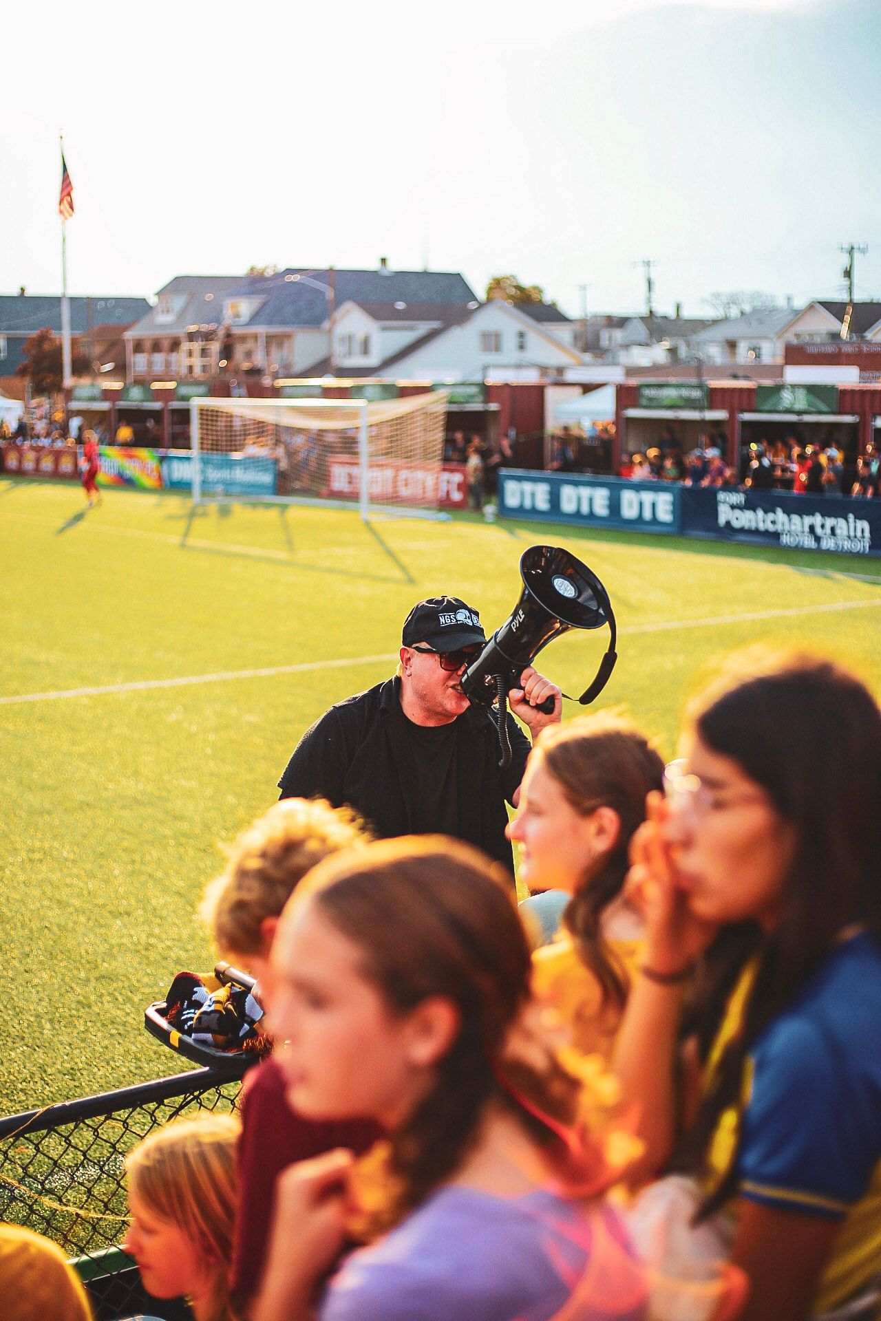 Man using a megaphone to lead cheers at a Detroit City FC soccer match on a sunny day.