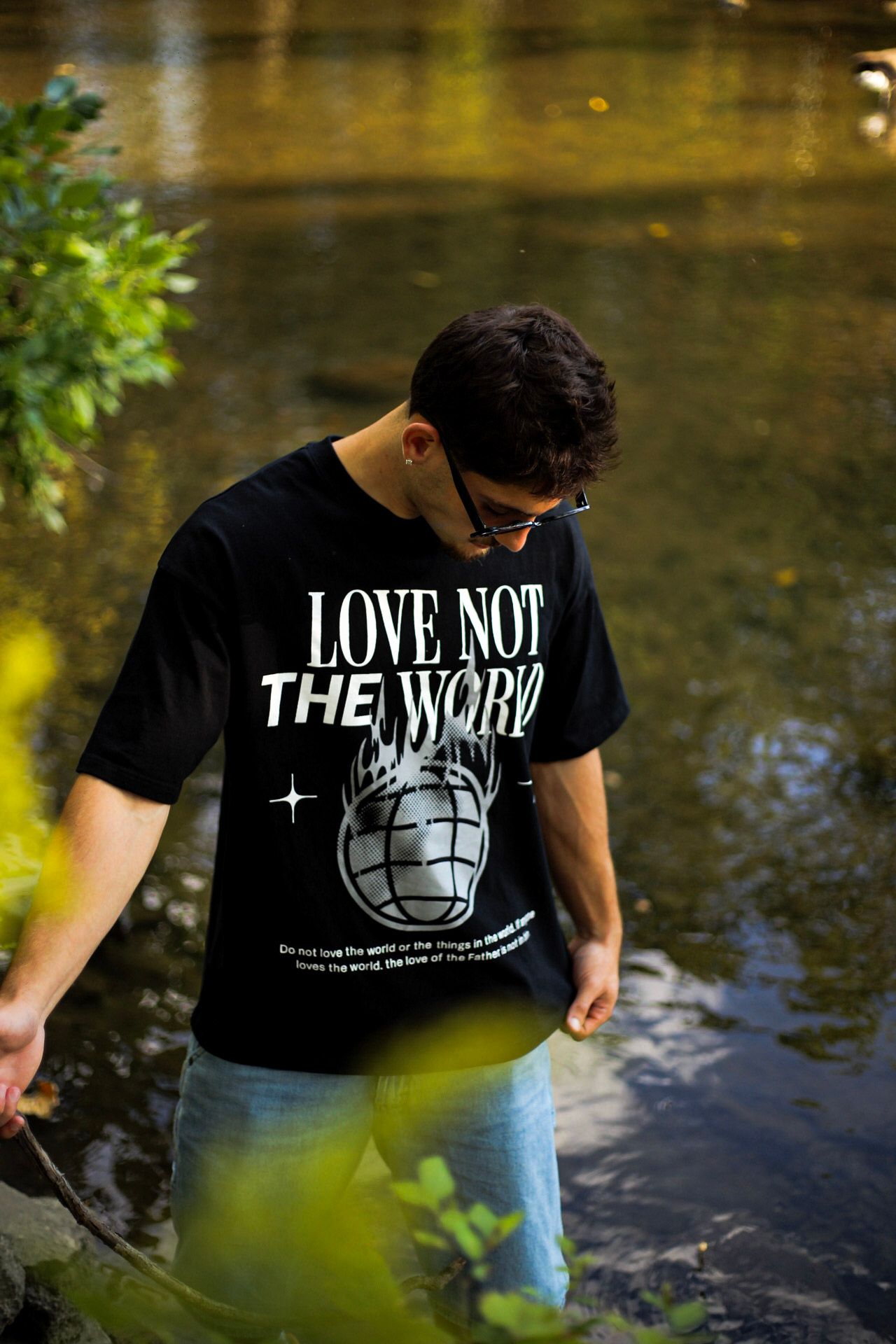 Man wading in river wearing black Love Not The World graphic tee with globe design and jeans.