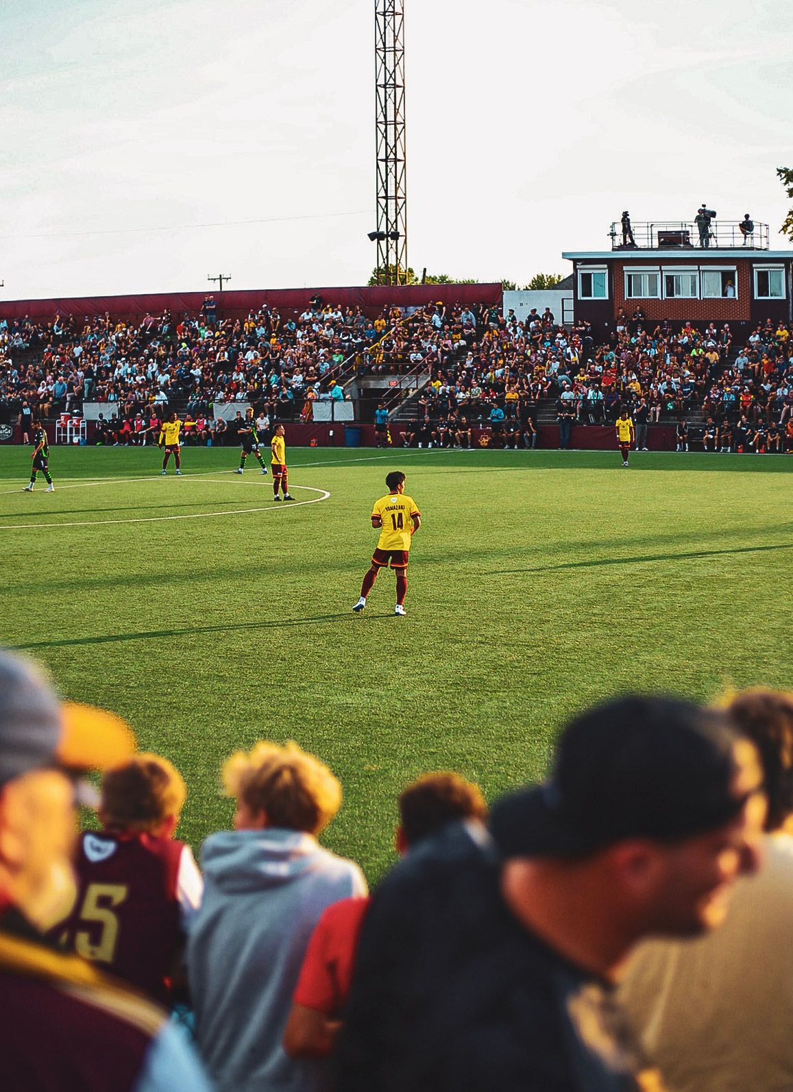 Detroit City FC soccer player in yellow jersey on field with packed stadium crowd in background.