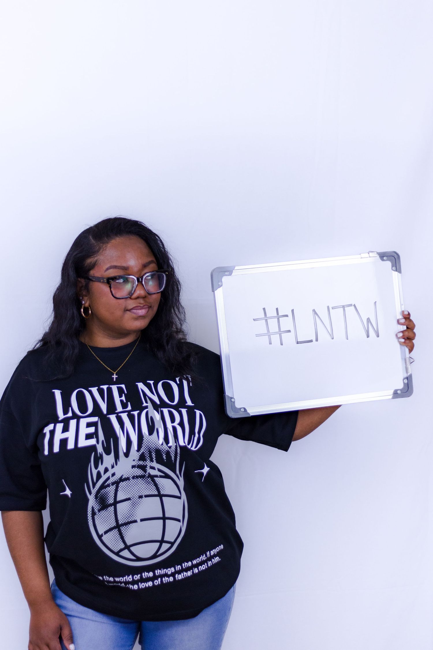 Woman holding whiteboard with #LNTW wearing black Love Not The World graphic tee.