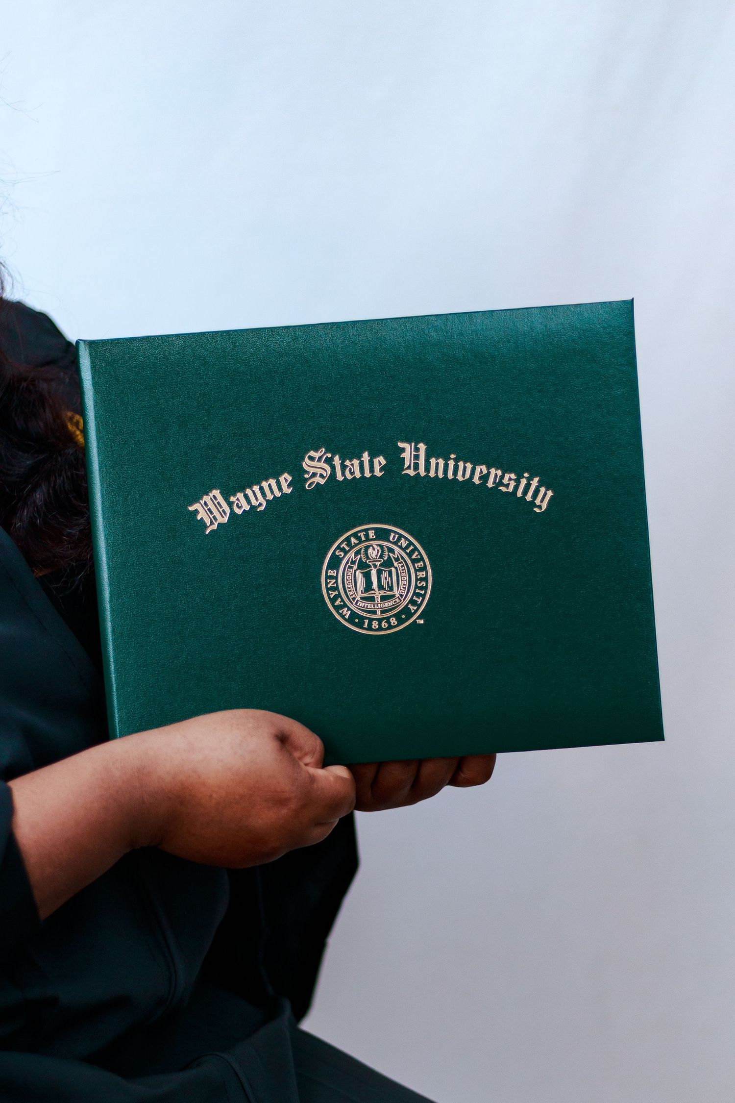Close-up of hands holding green Wayne State University diploma cover with gold emblem.