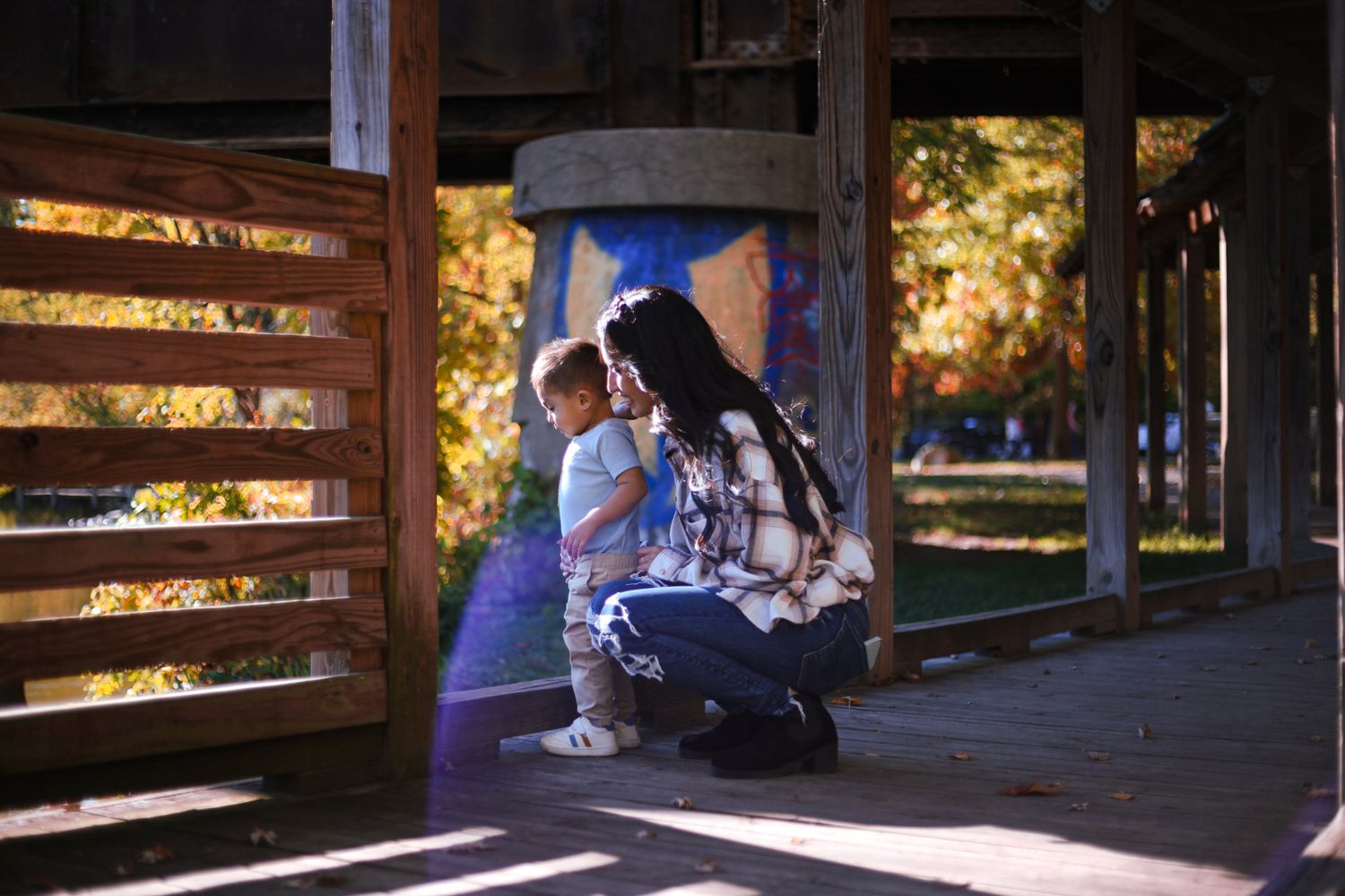 Woman crouching with young child under covered structure in sunlight.