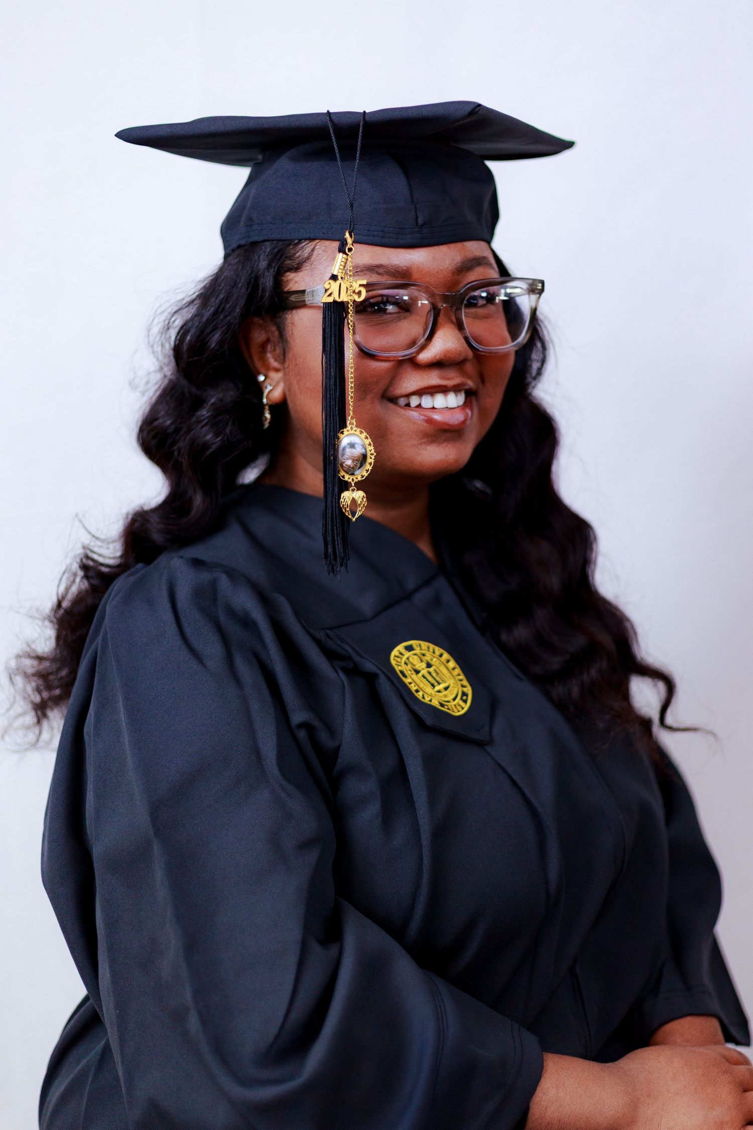 Smiling woman in black graduation cap and gown with glasses celebrating academic achievement.