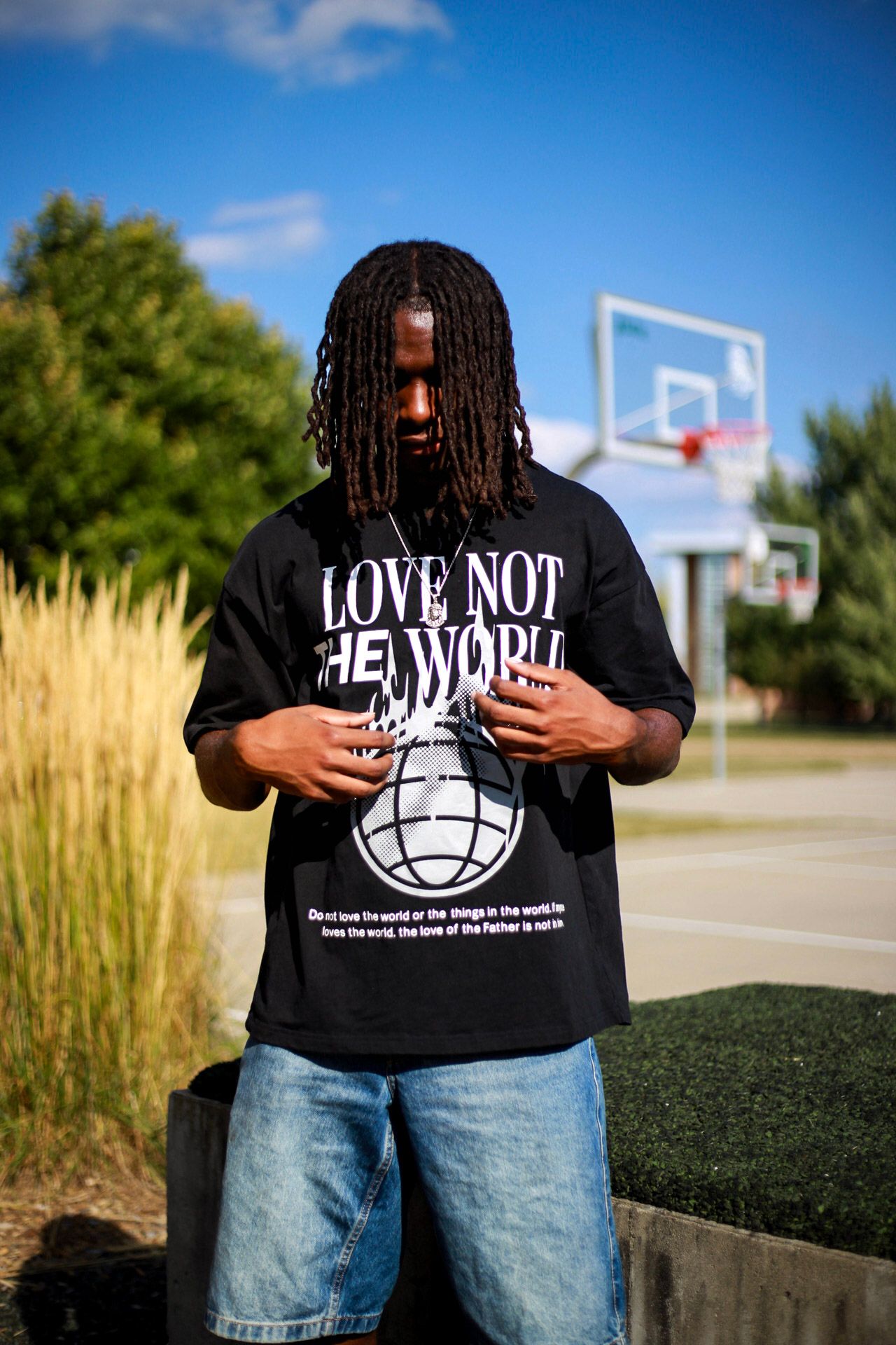 Man in black 'Love Not The World' graphic tee and jeans looking down near basketball court.
